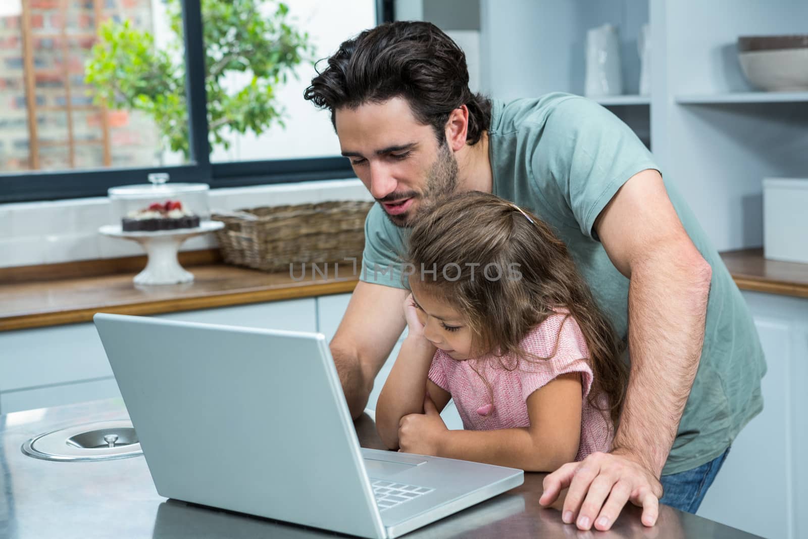 Smiling father using laptop with his daughter in the kitchen at home