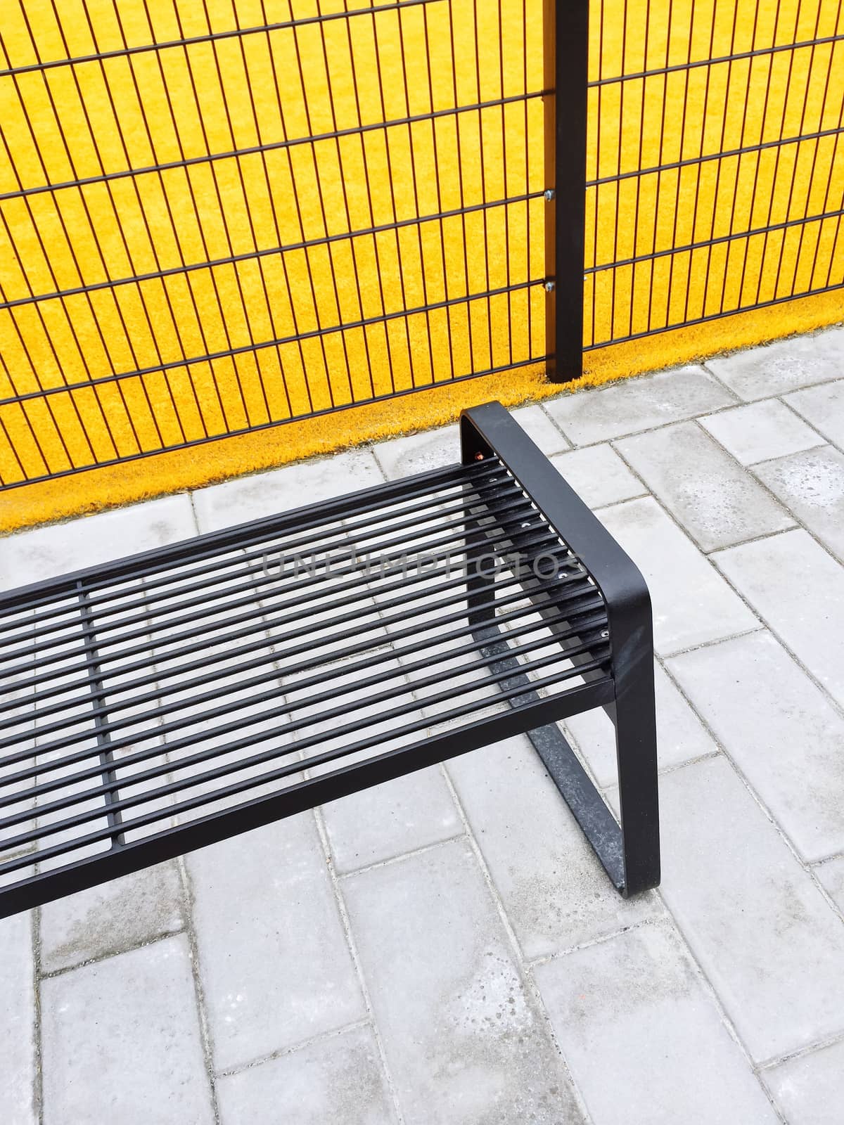 Metal bench near bright yellow playground. Urban architecture.