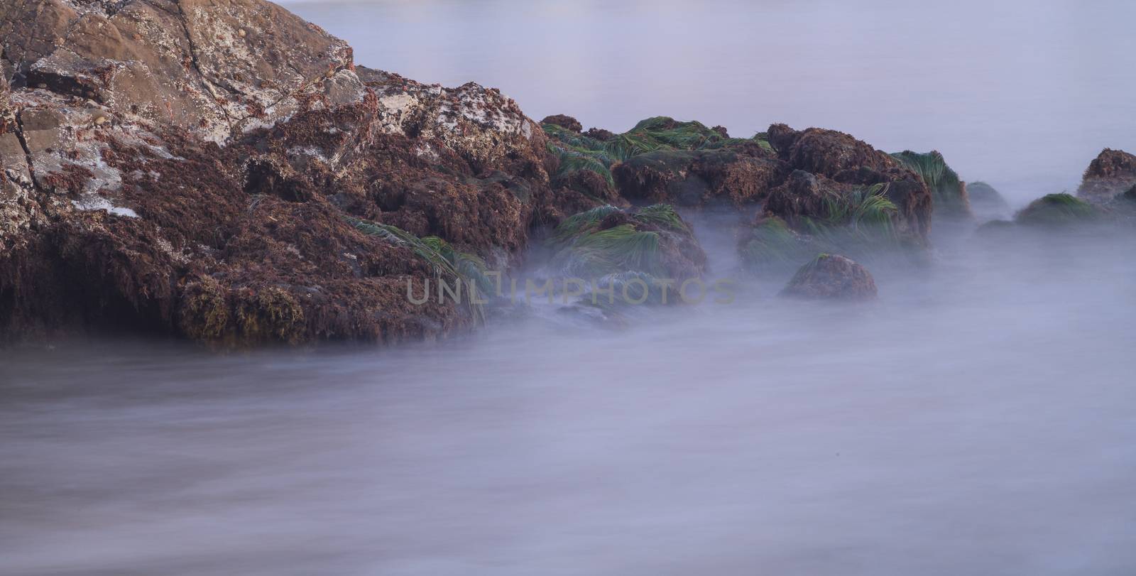 Long exposure of sunset over rocks, giving a mist like effect over ocean in Laguna Beach, California