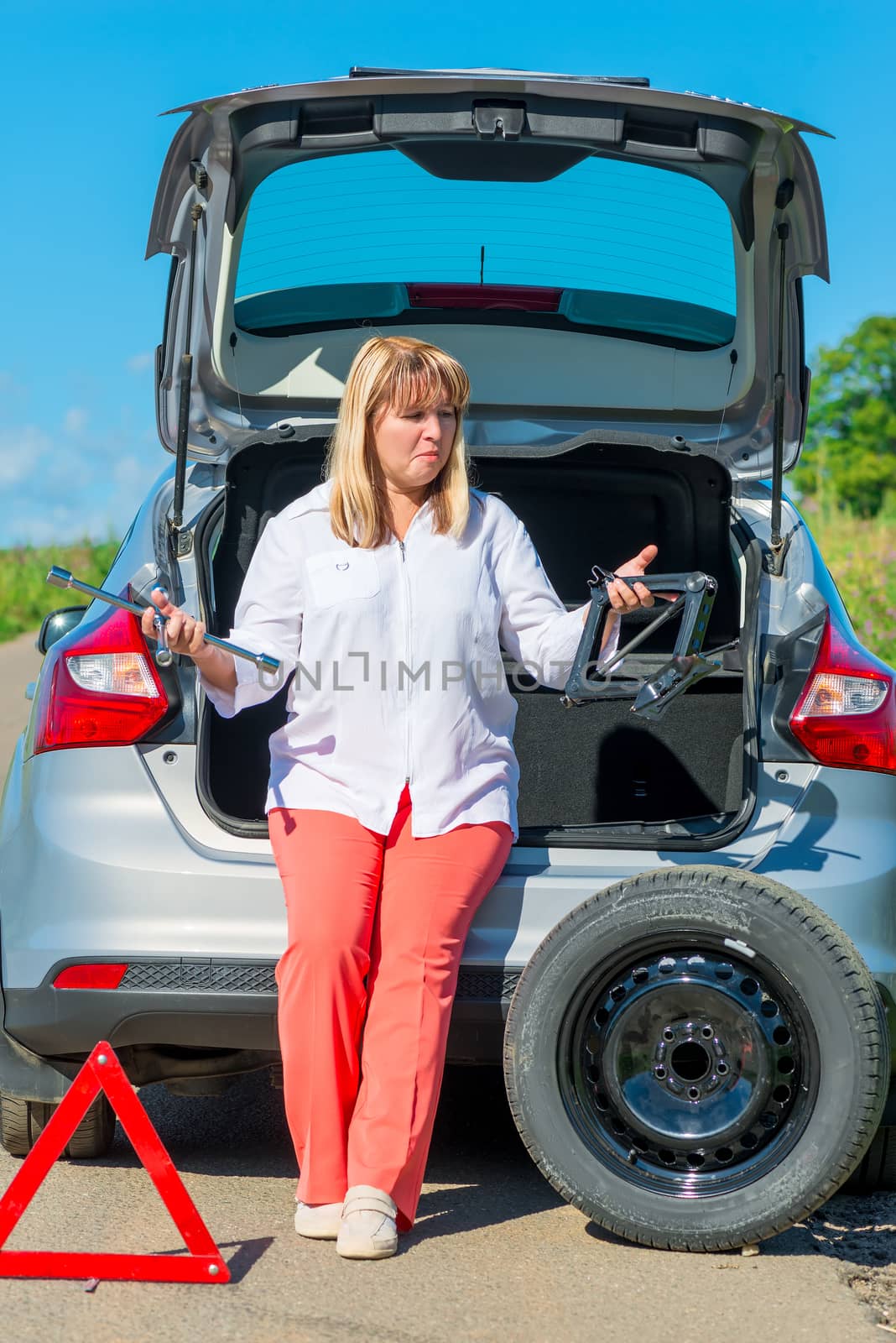 confused mature woman driver near his car going to change wheels