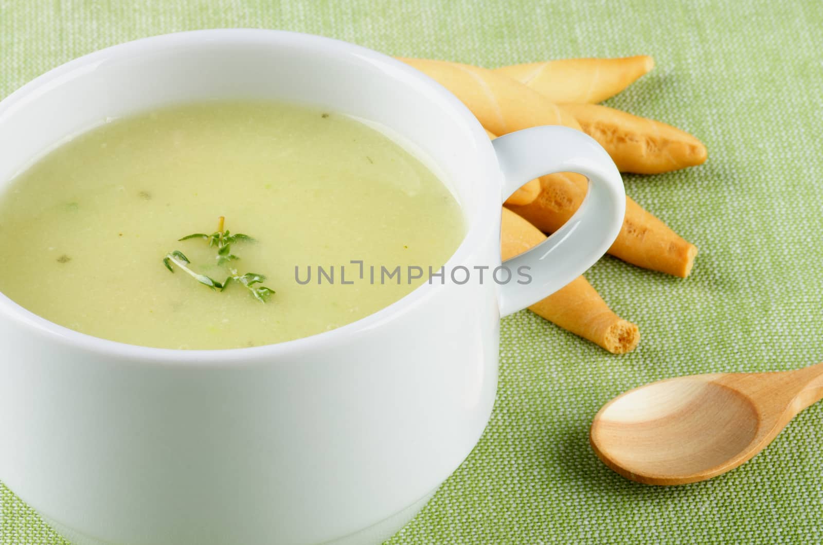 Delicious Cream Asparagus Soup in White Soup Cup with Bread Sticks and Wooden Spoon Cross Section on Green Napkin