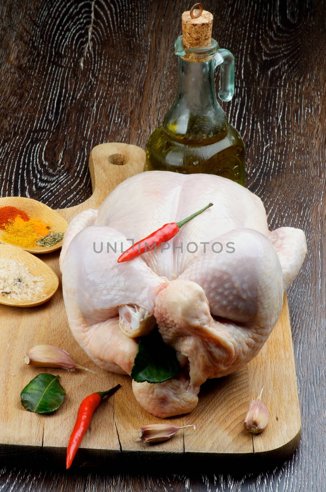 Perfect Raw Chicken Full Body Trussed and Ready to Roast with Hot Crushed Spices, Chili Peppers, Garlic, Curry Leaves and Olive Oil closeup on Wooden Cutting Board