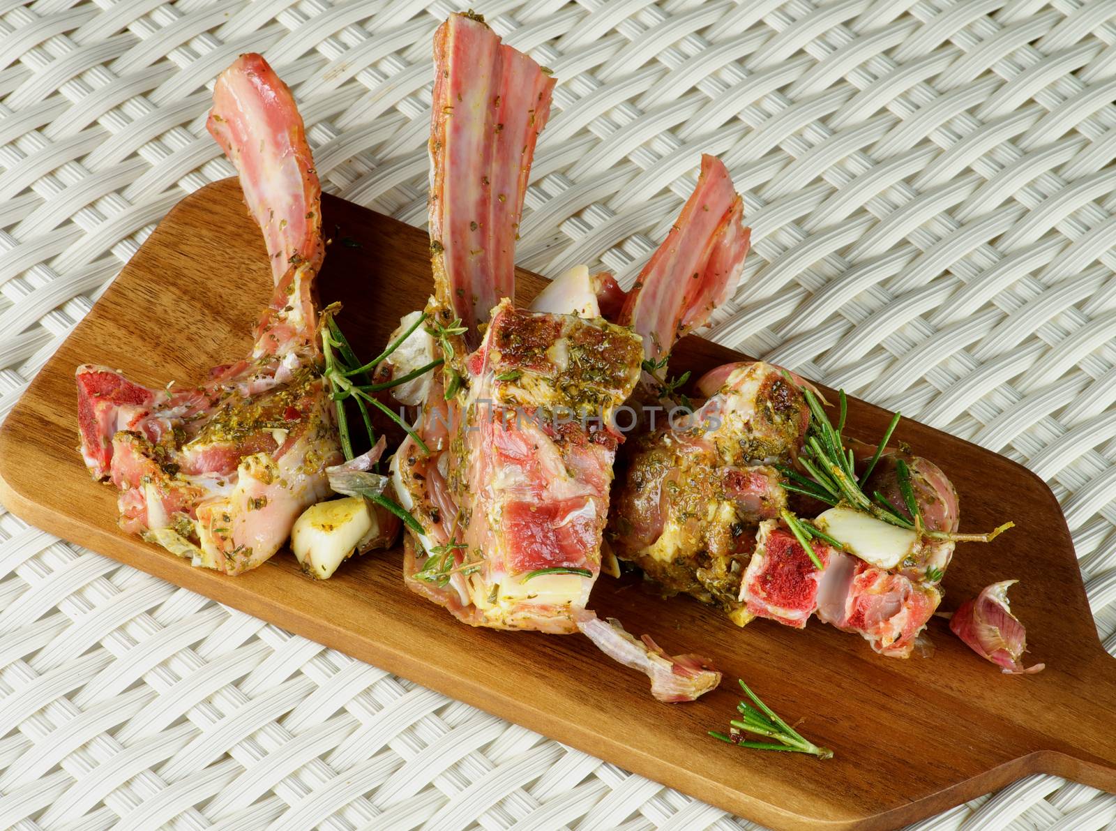 Raw Lamb Ribs in Marinade of Herbs with Rosemary and Garlic closeup on Wooden Cutting Board on Wicker background. Top View