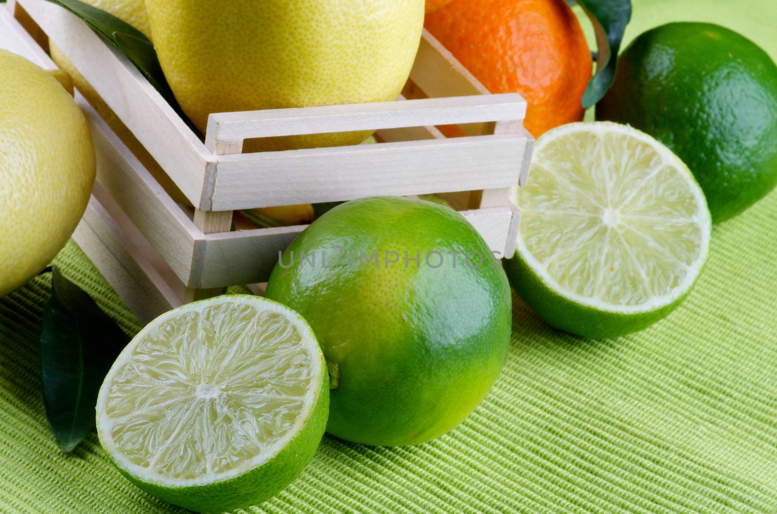 Heap of Various Citrus Fruits with Full Body Lemons, Tangerine and Limes Full Body and Halves in Wooden Box closeup on Green Napkin background
