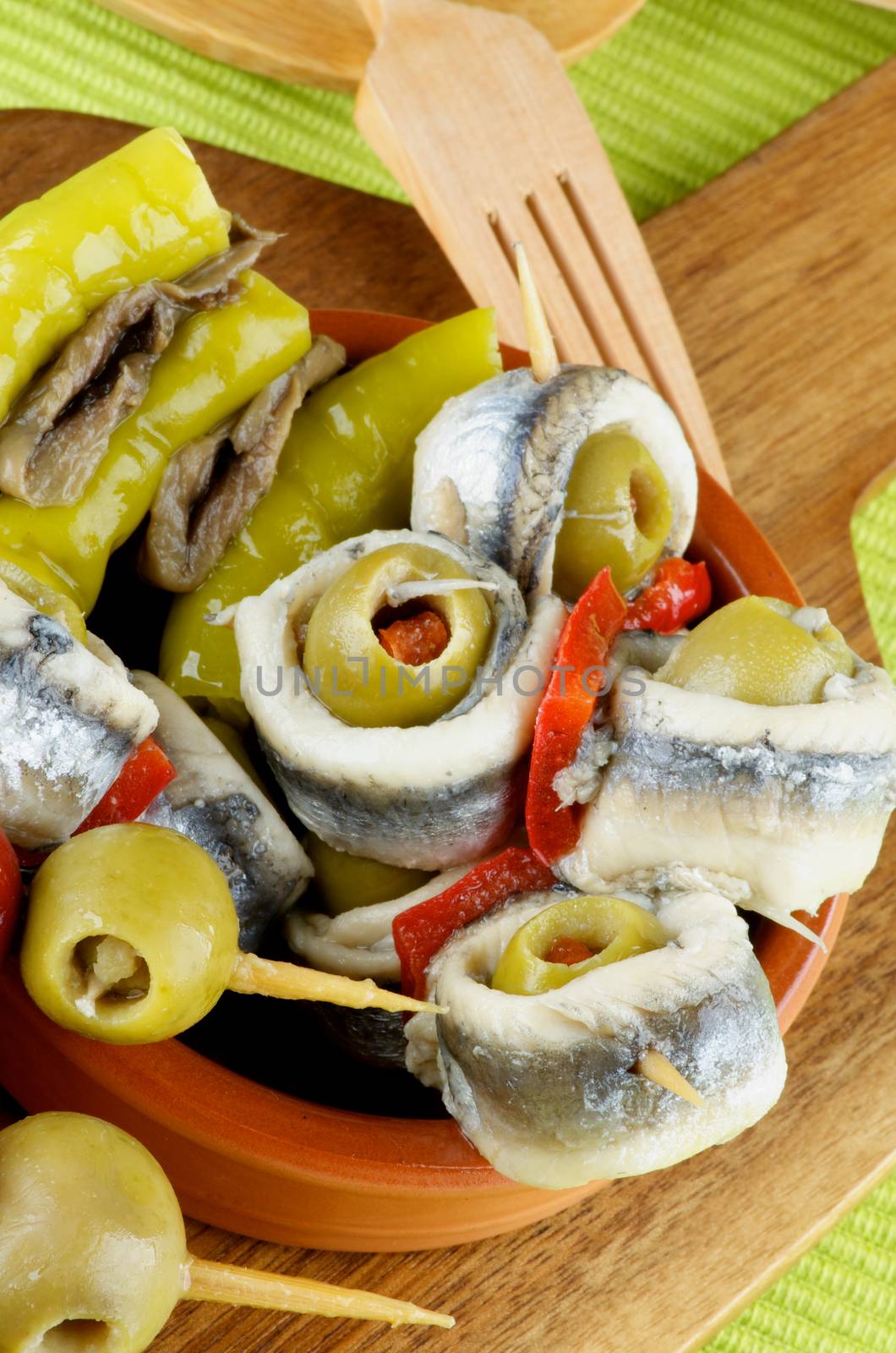 Delicious Spanish Snacks with Marinated Peppers, Anchovies and Green Olives  with Wooden Fork closeup on Wooden Cutting Board