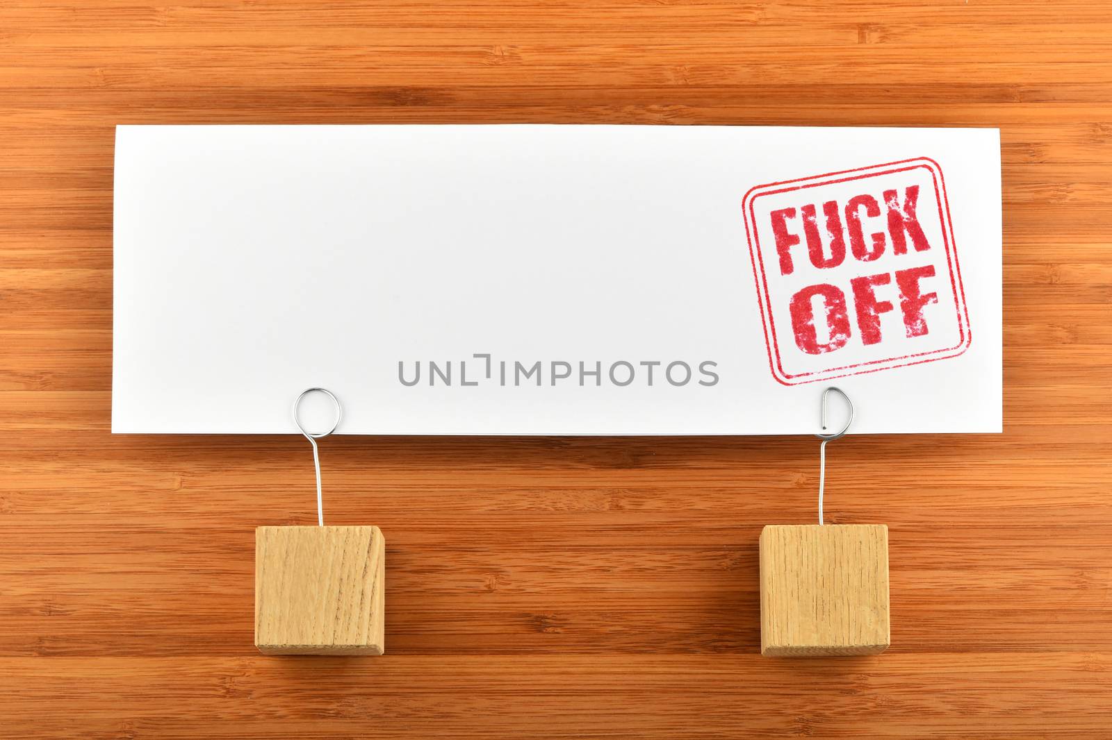 Fuck off red rude stamp on one big white paper note with two wooden holders on wooden bamboo background for presentation