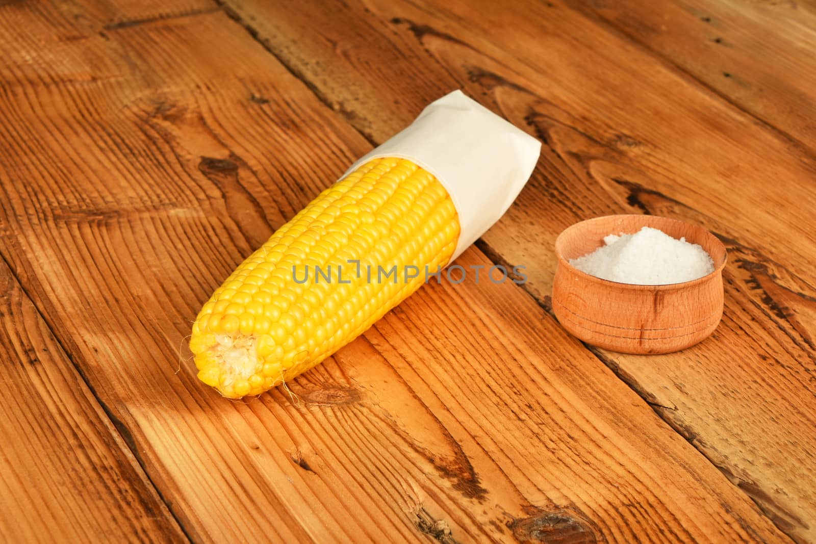 One open fresh yellow corn cob and salt in cup on brown vintage wooden surface