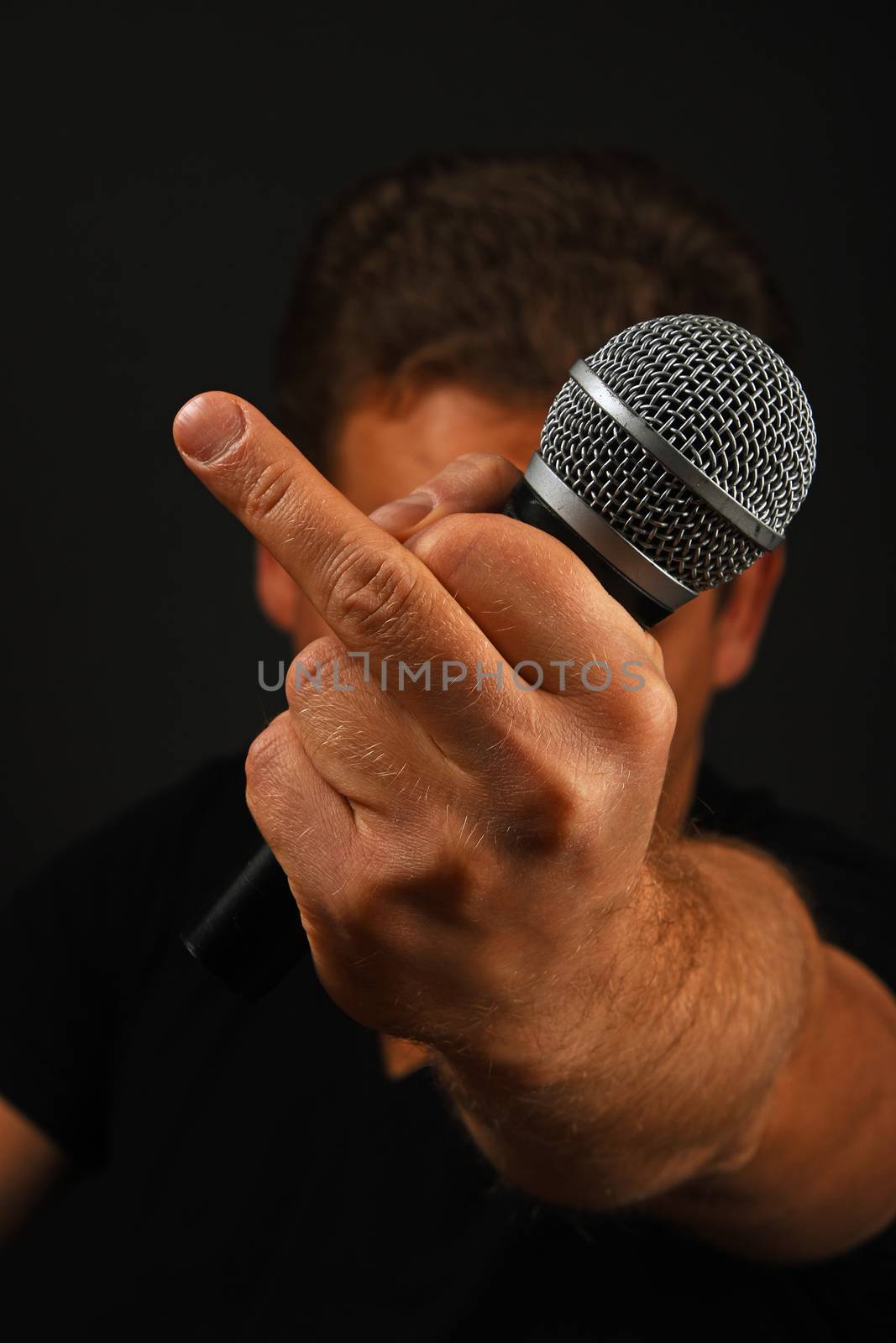 Male hand holding microphone with finger fuck off insult ignore gesture with head behind on black background
