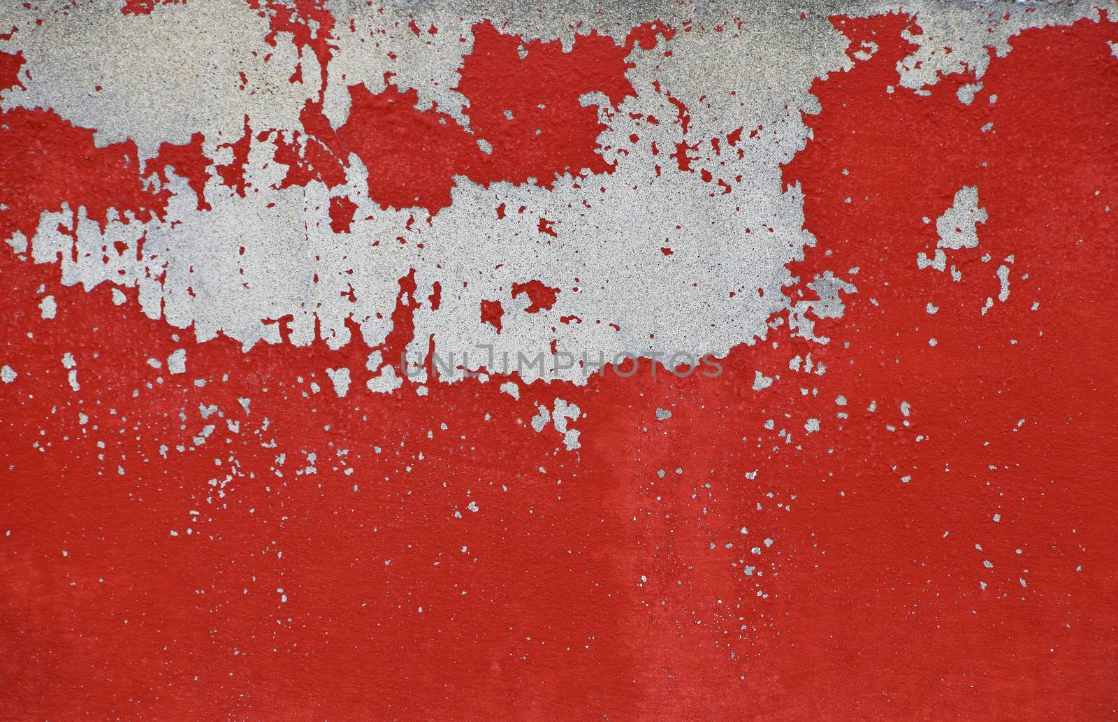 Flakes of old vintage grungy bright vivid red paint on grey concrete wall