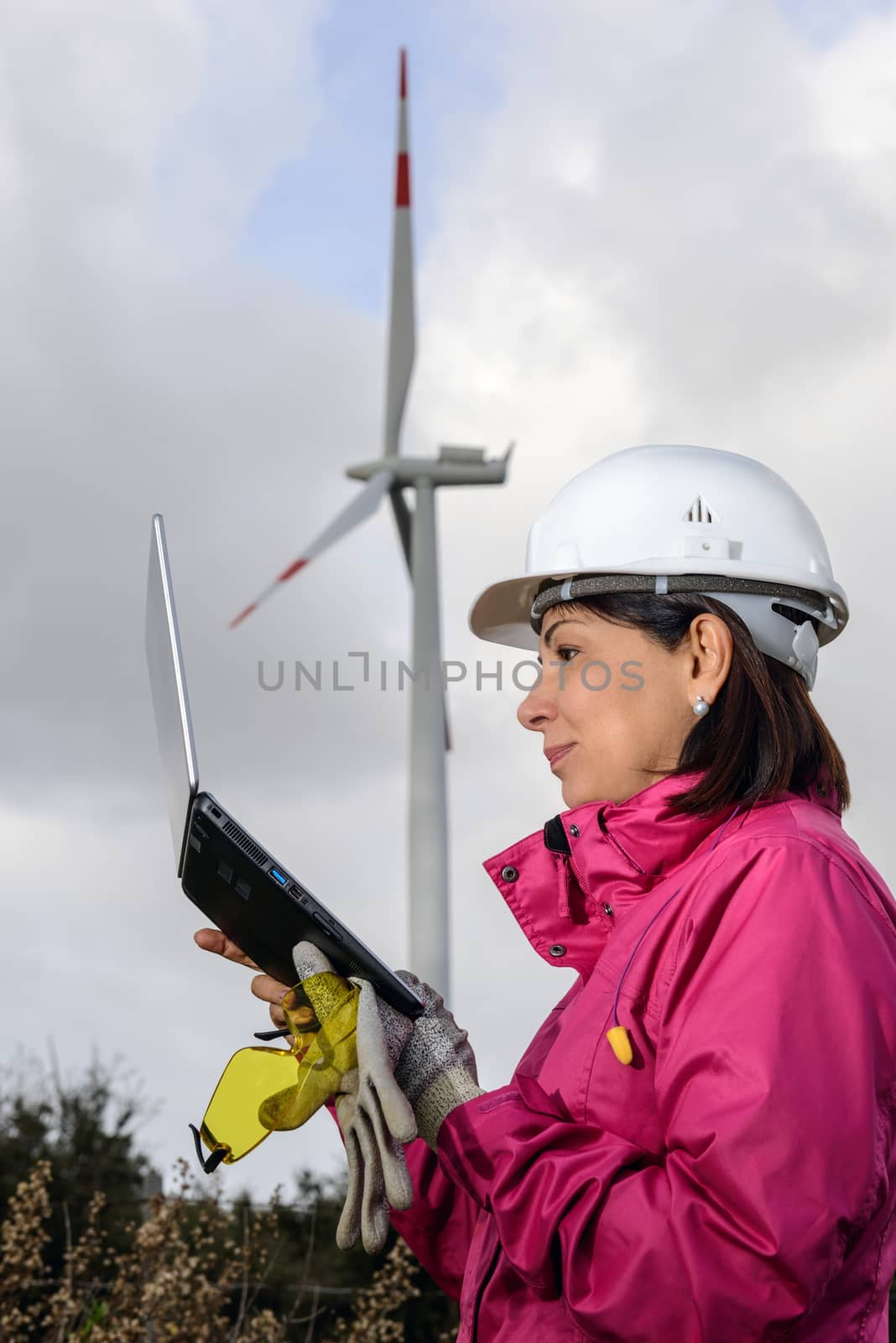 Engineer woman checking production, with laptops, wind turbines on the site.