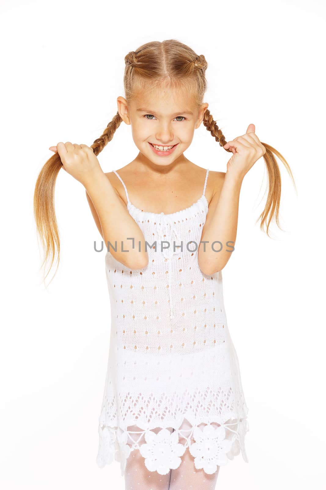 Funny little girl with a charming smile in a white dress holding a pigtails