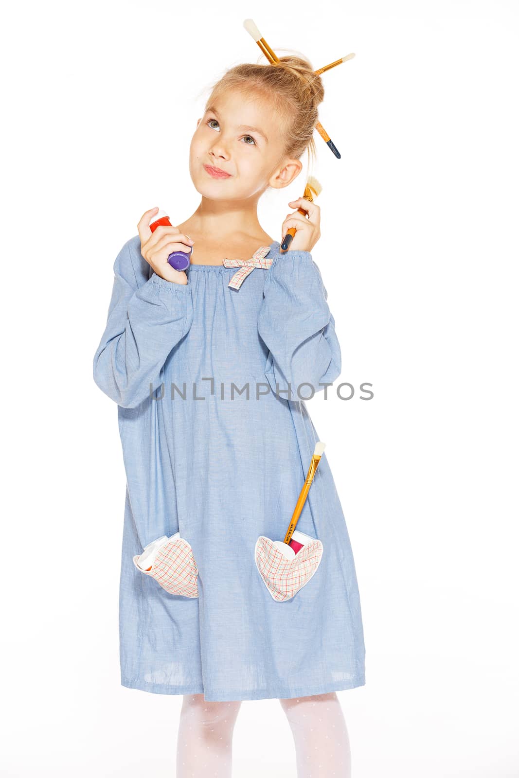 Little girl painter in a blue dress with paints and brushes