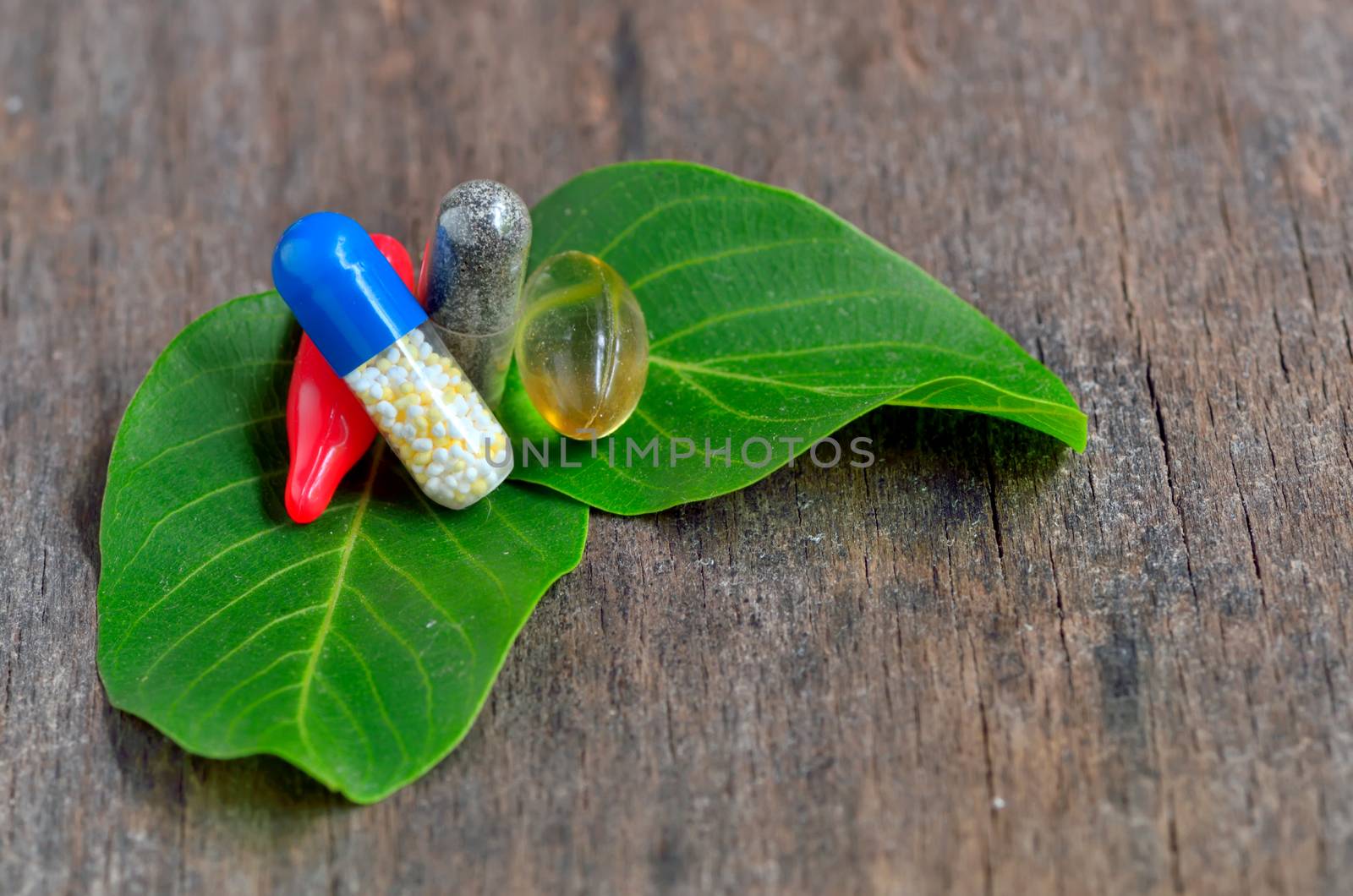 Herb capsule on leaves on wooden background