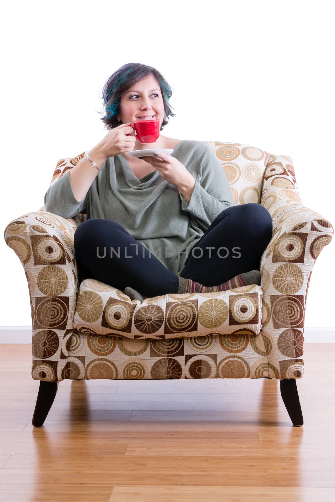 Pleased middle-aged woman at home sitting comfortably in sofa chair enjoying her morning coffee