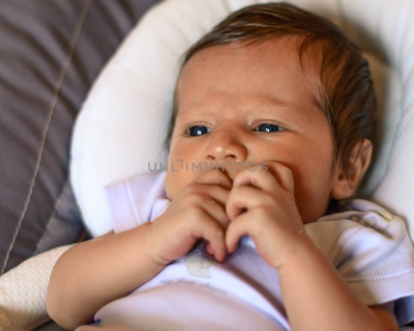 Thoughtful newborn boy looking left side with concentrated look and hand in the mouth,in his crib.