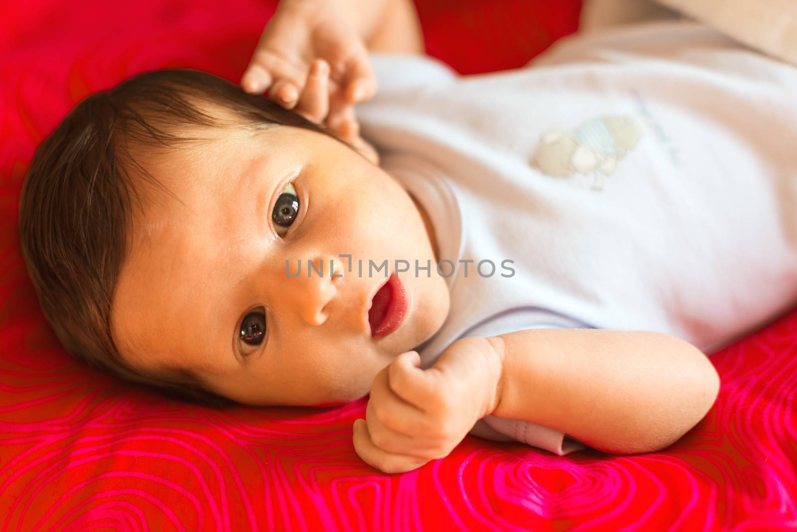 Newborn boy looks surprised with his mouth open on a red background.
