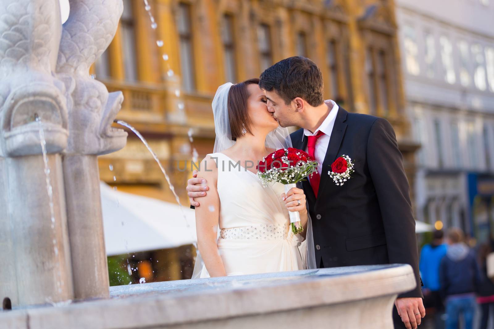 Bride and groom. Portrait of a loving wedding couple kissing by the fountain in medieval city center of Ljubljana, Slovenia.