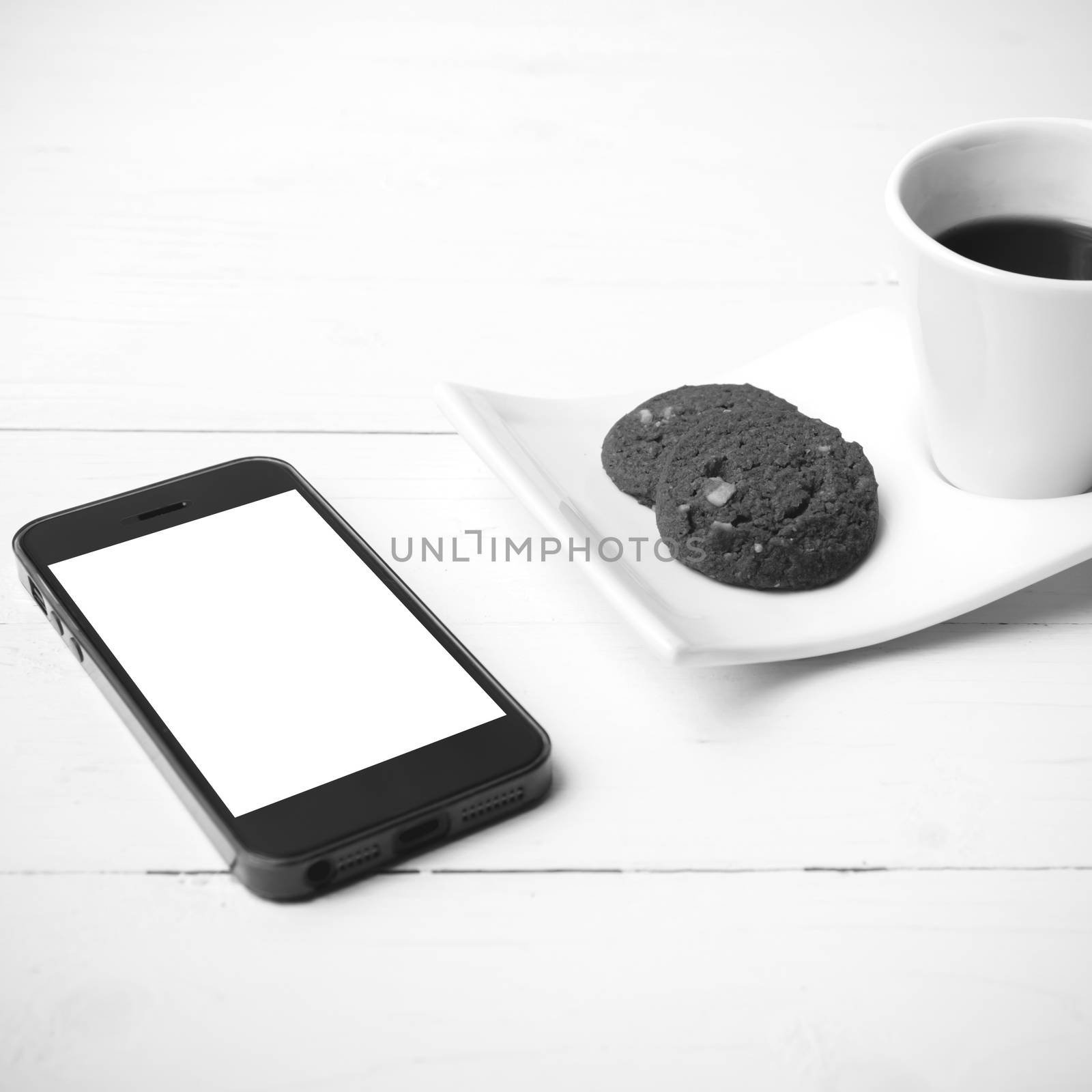 coffee cup with cookie and phone on white wood black and white color