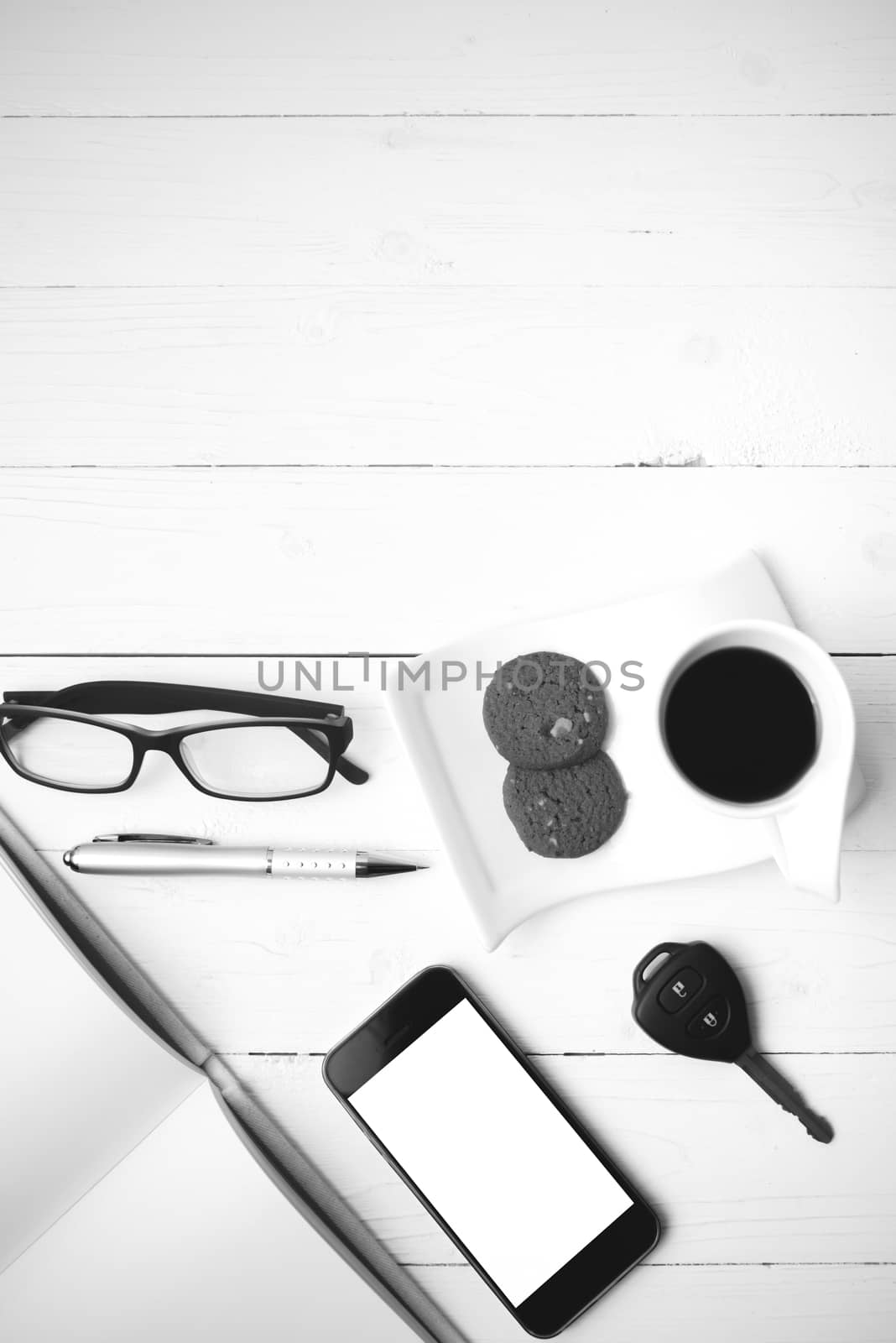 coffee cup with cookie,phone,open notebook,car key and eyeglasses on white wood table black and white color