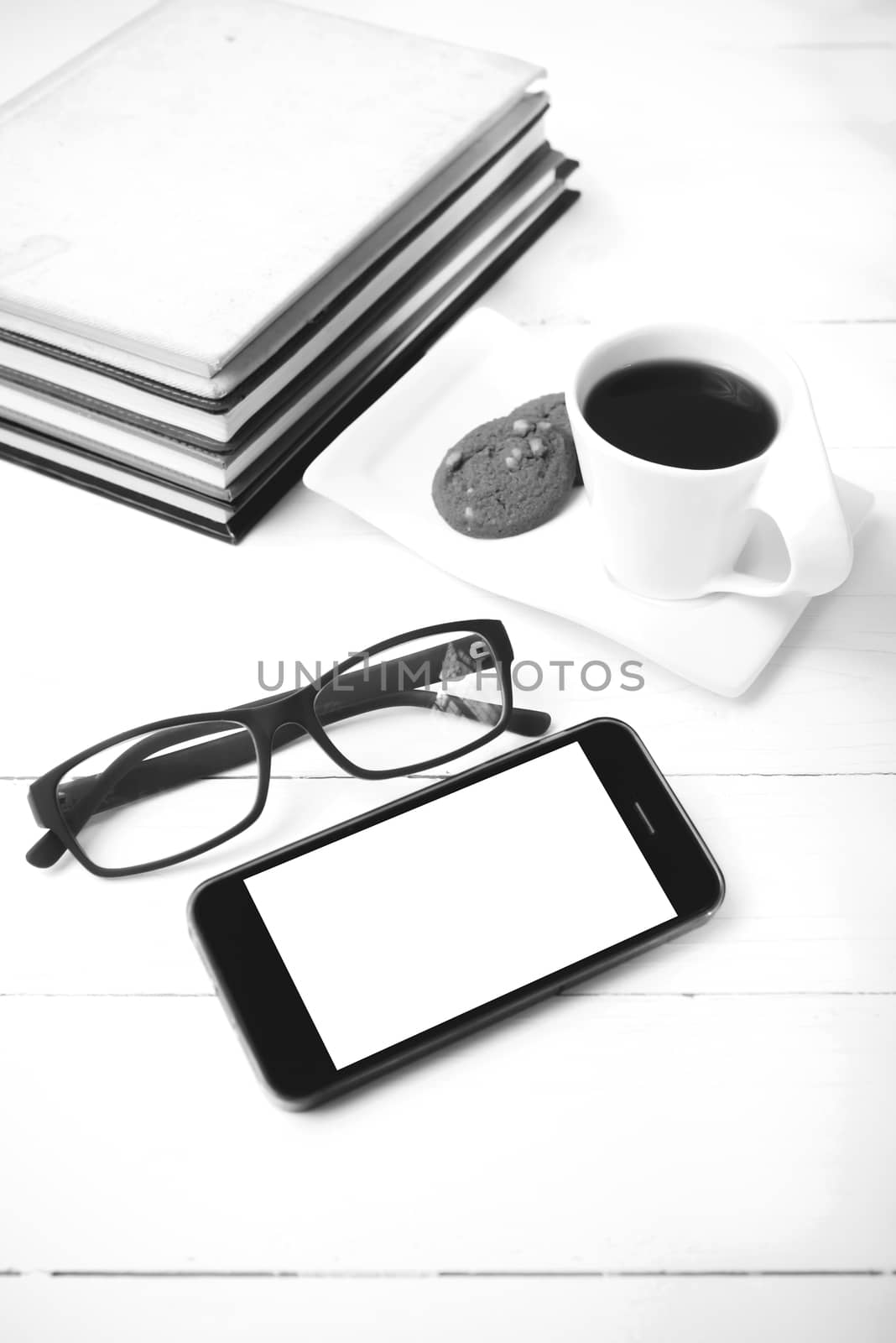 coffee cup with cookie,phone,stack of book and eyeglasses on white wood table black and white color