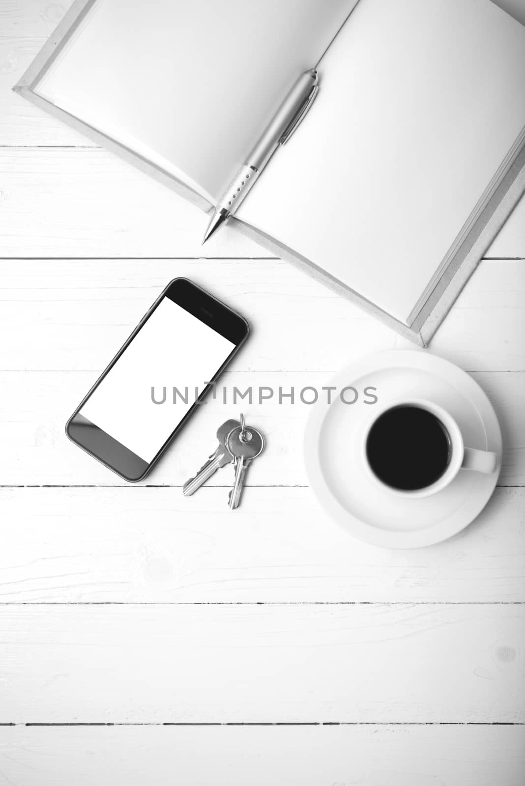 coffee cup with phone, key and open notebook on white wood table black and white color
