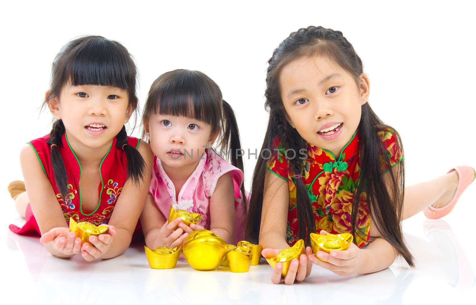 China girls in traditional Chinese cheongsam dress greeting, holding a gold ingot lying down in the studio