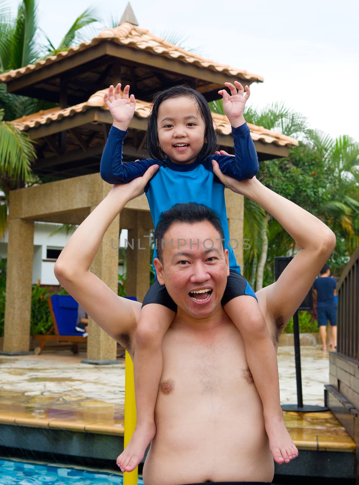 Man carrying his little daughter on shoulders in swimming pool 