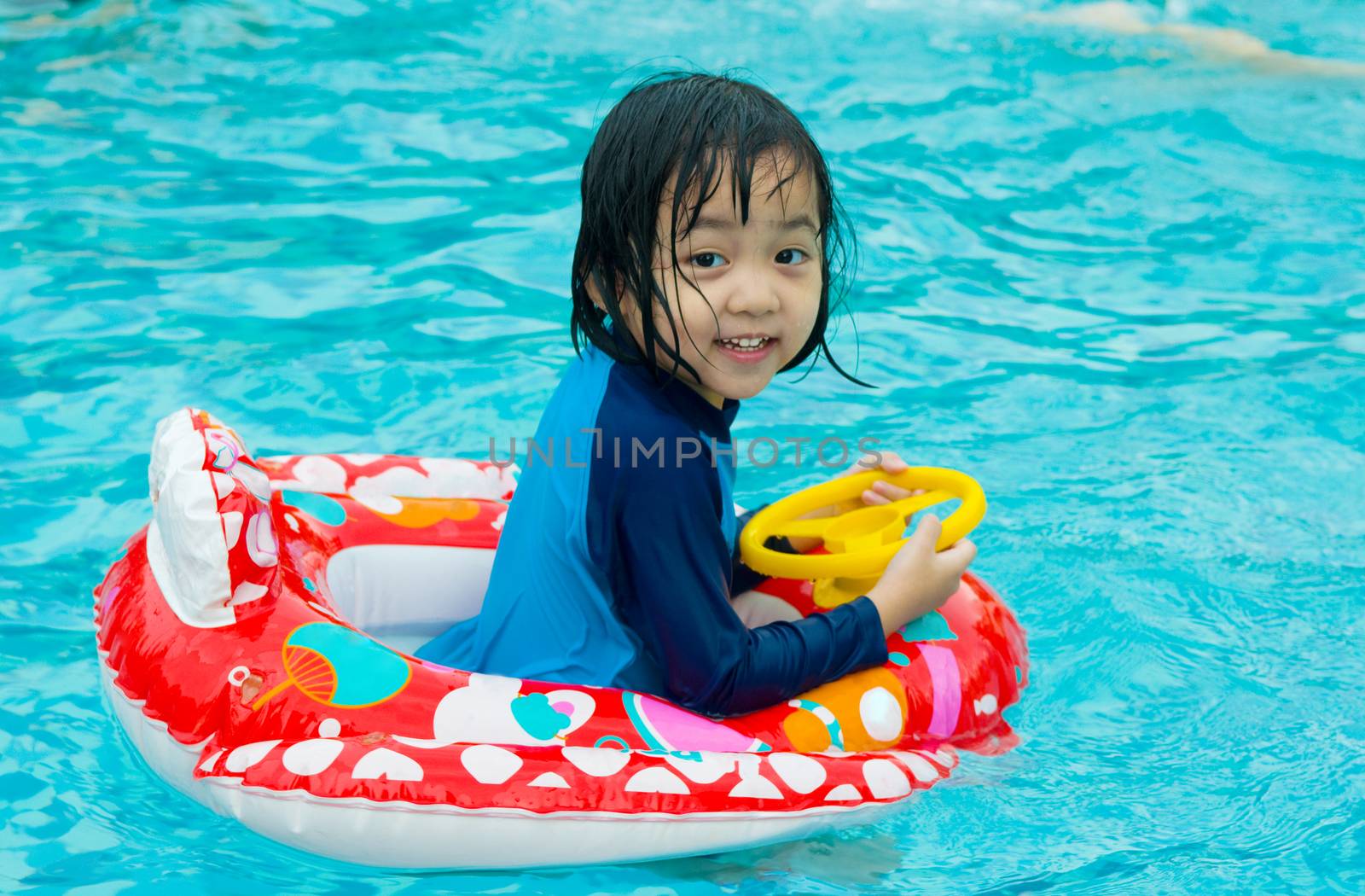 asian child in swim tube playing on swimming pool