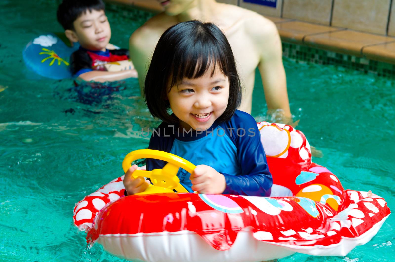 asian child in swim tube playing on swimming pool