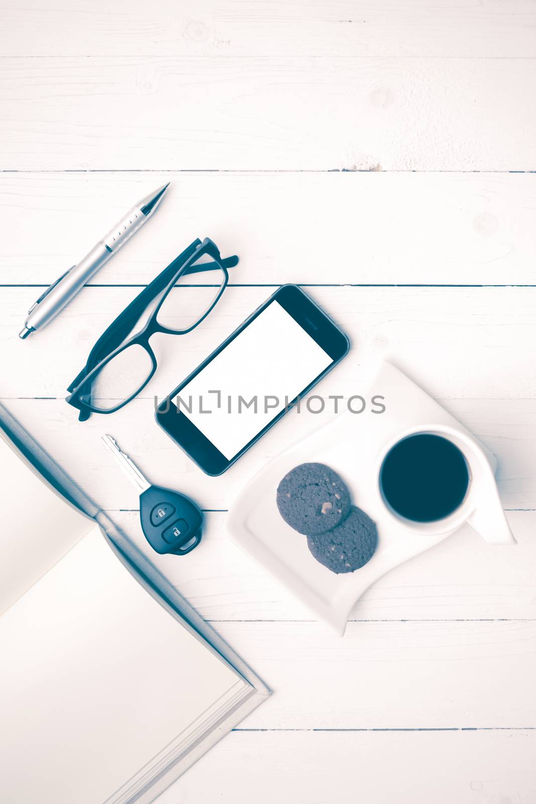 coffee cup with cookie,phone,open notebook,car key and eyeglasses on white wood table vintage style