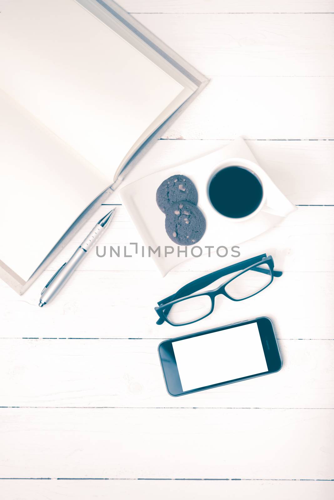 coffee cup with cookie,phone,notebook and eyeglasses on white wood table vintage style