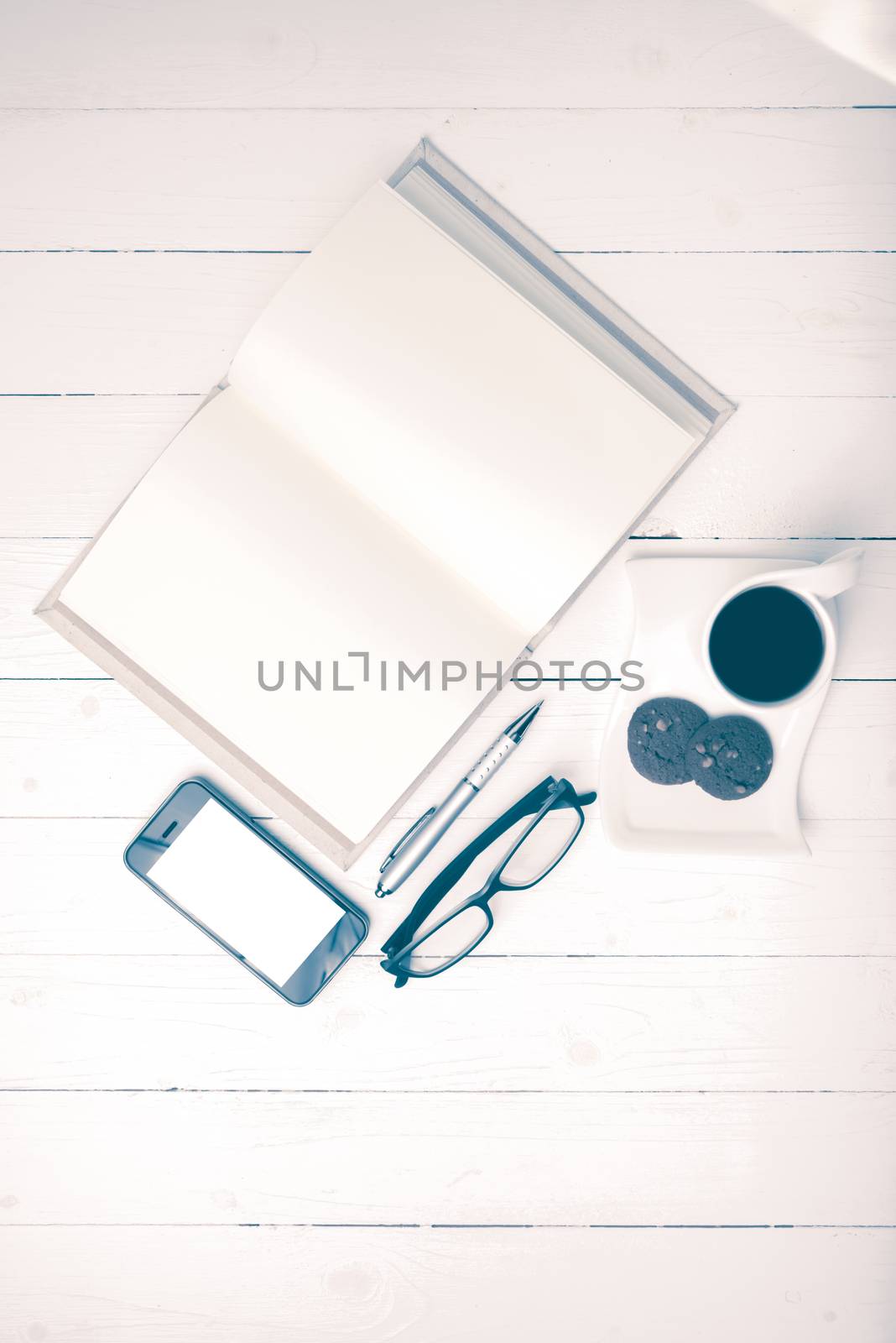 coffee cup with cookie,phone,notebook and eyeglasses on white wood table vintage style