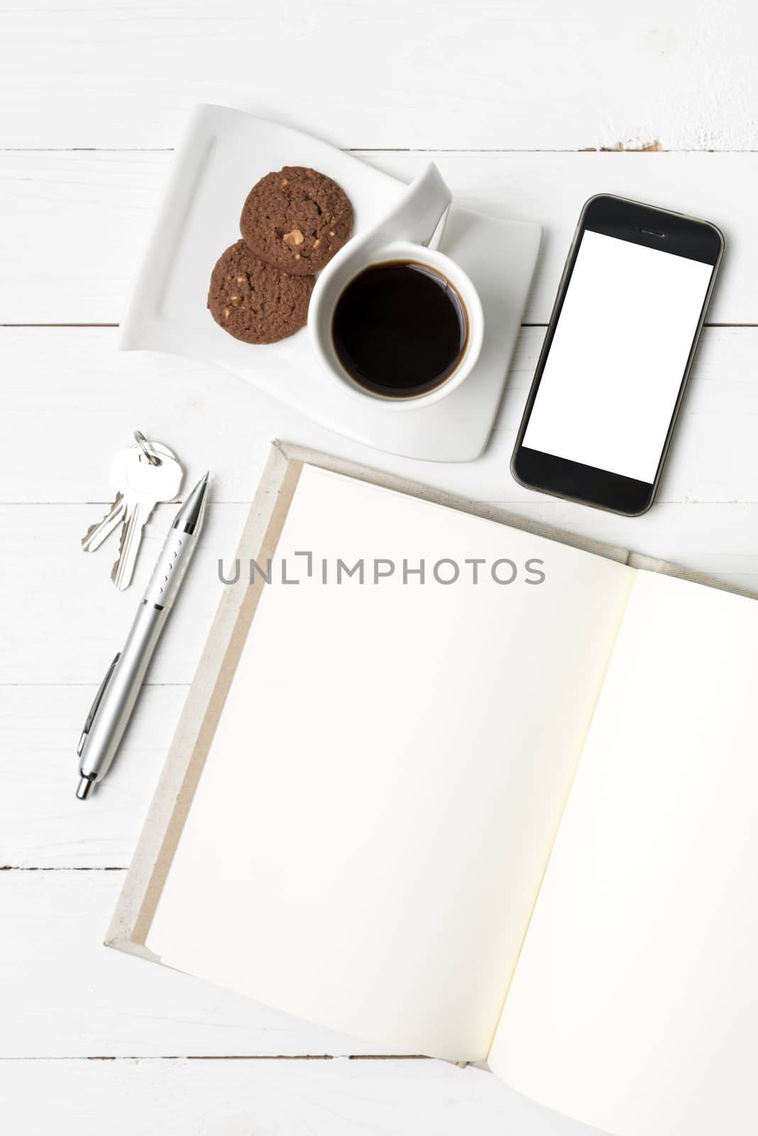 coffee cup with cookie,phone,notebook and key on white wood table