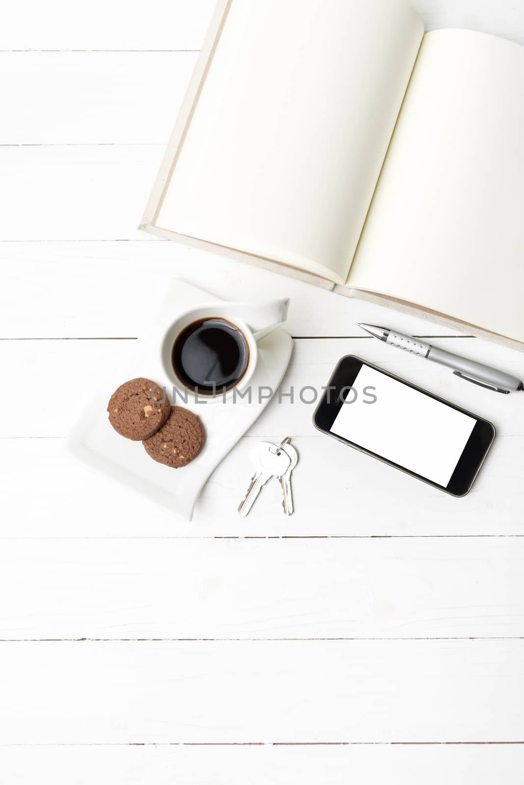 coffee cup with cookie,phone,notebook and key on white wood table