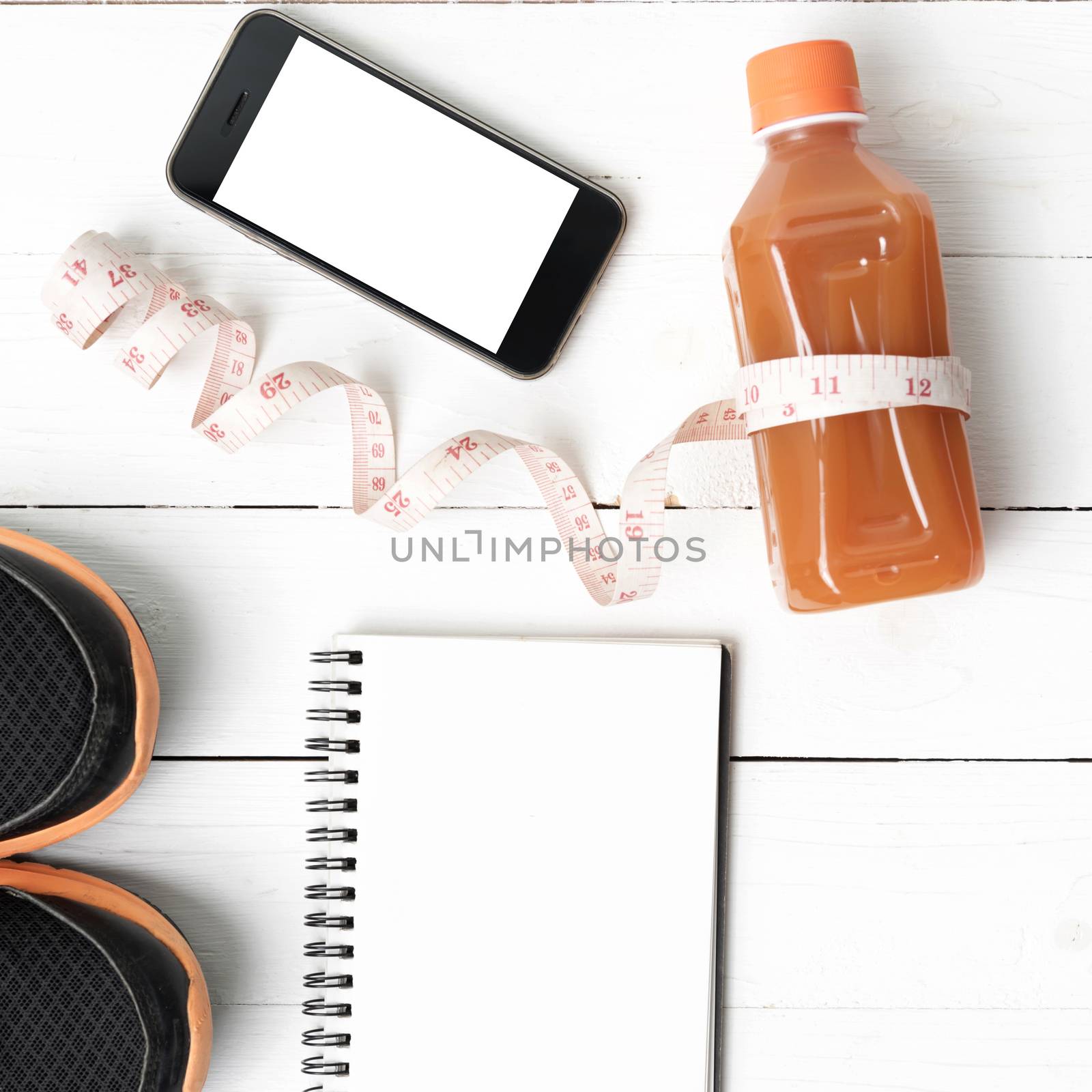 fitness equipment:running shoes,juice,measuring tape,notepad and phone on white wood background