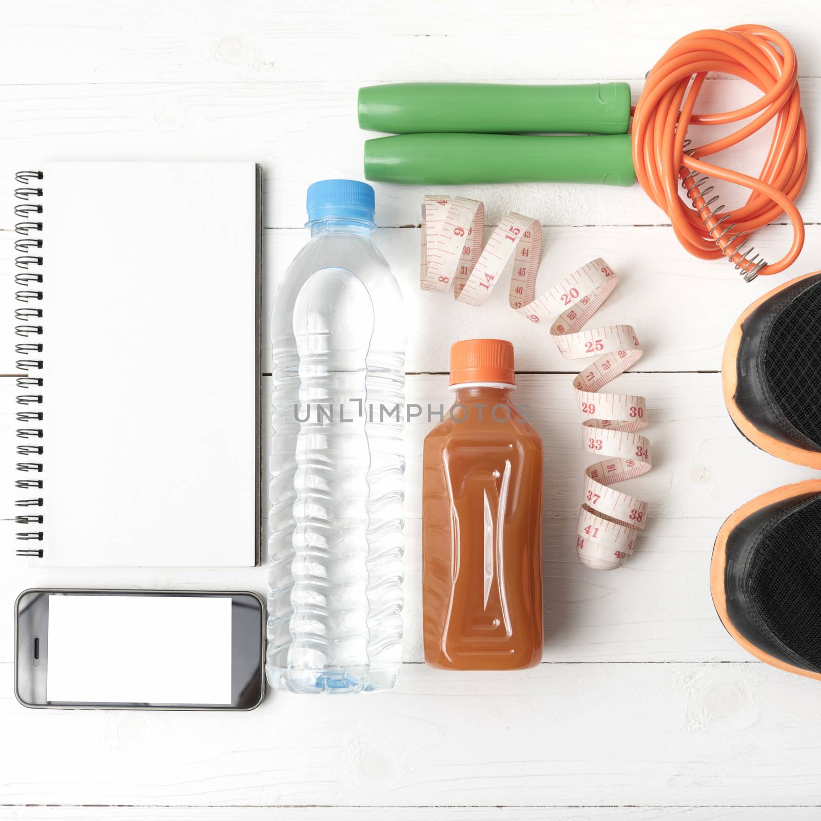 fitness equipment:running shoes,jumping rope,notepad,phone,water,juice and measuring tape on white wood background