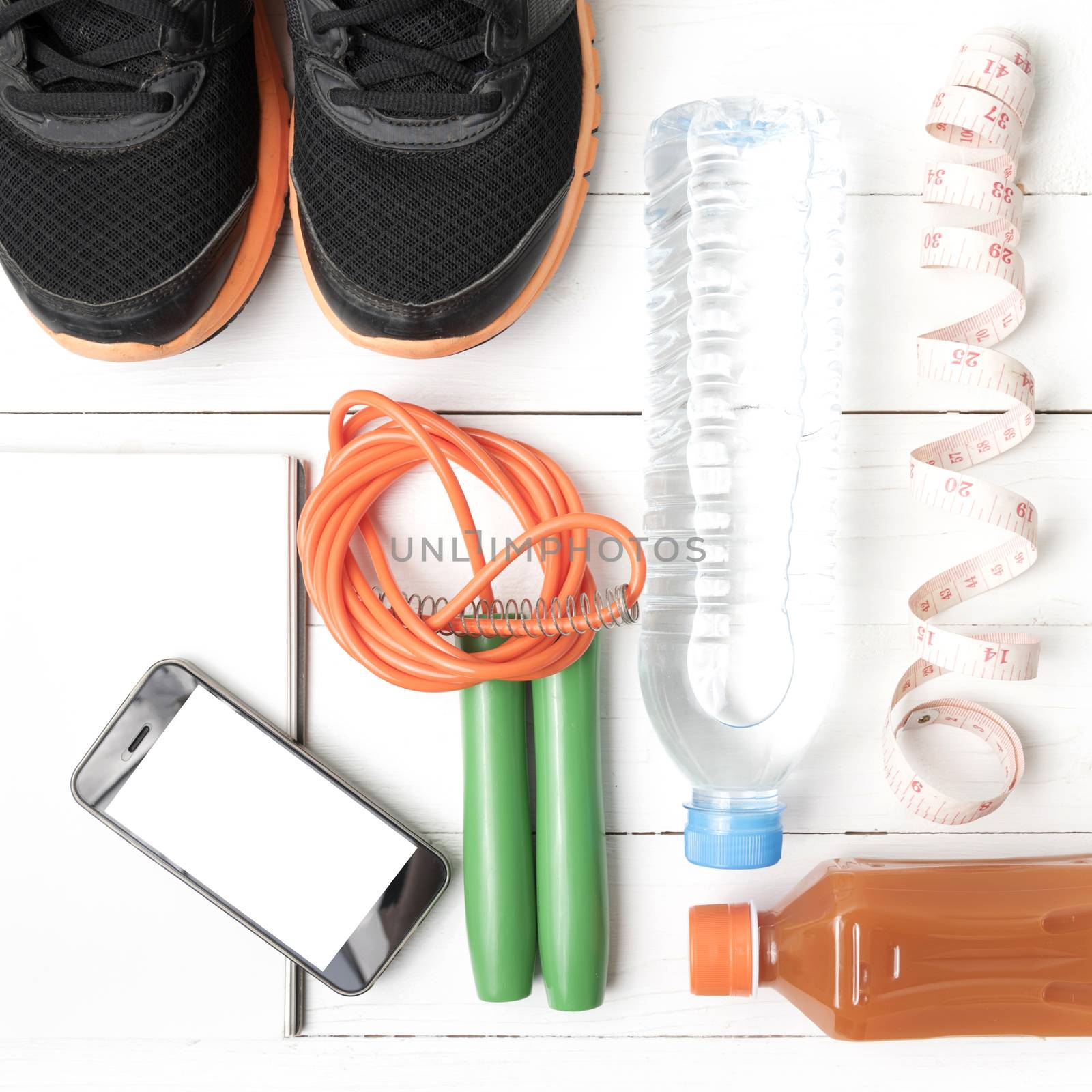 fitness equipment:running shoes,jumping rope,notepad,phone,water,juice and measuring tape on white wood background