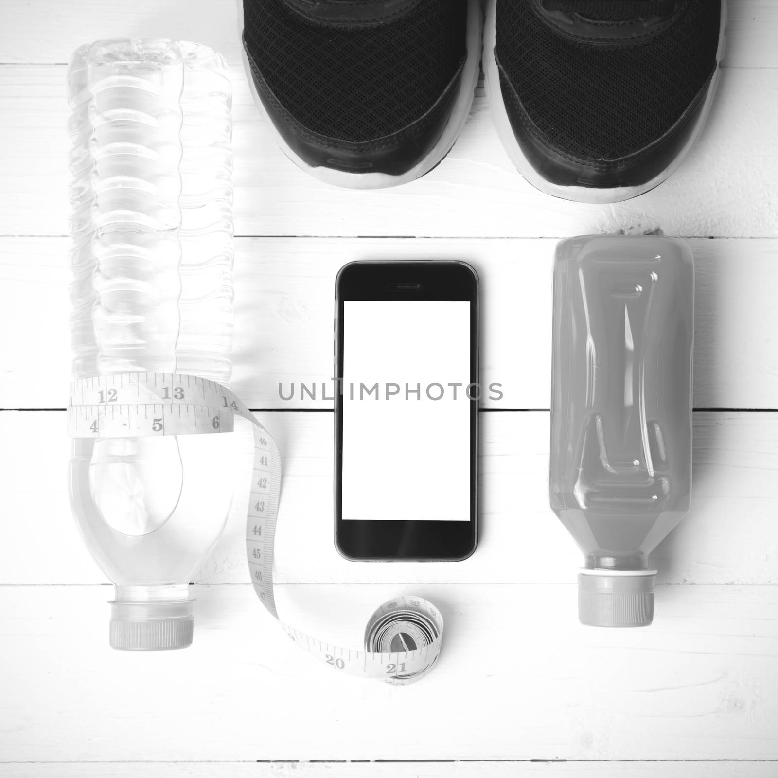 fitness equipment:running shoes,measuring tape,water,juice and phone on white wood background black and white color