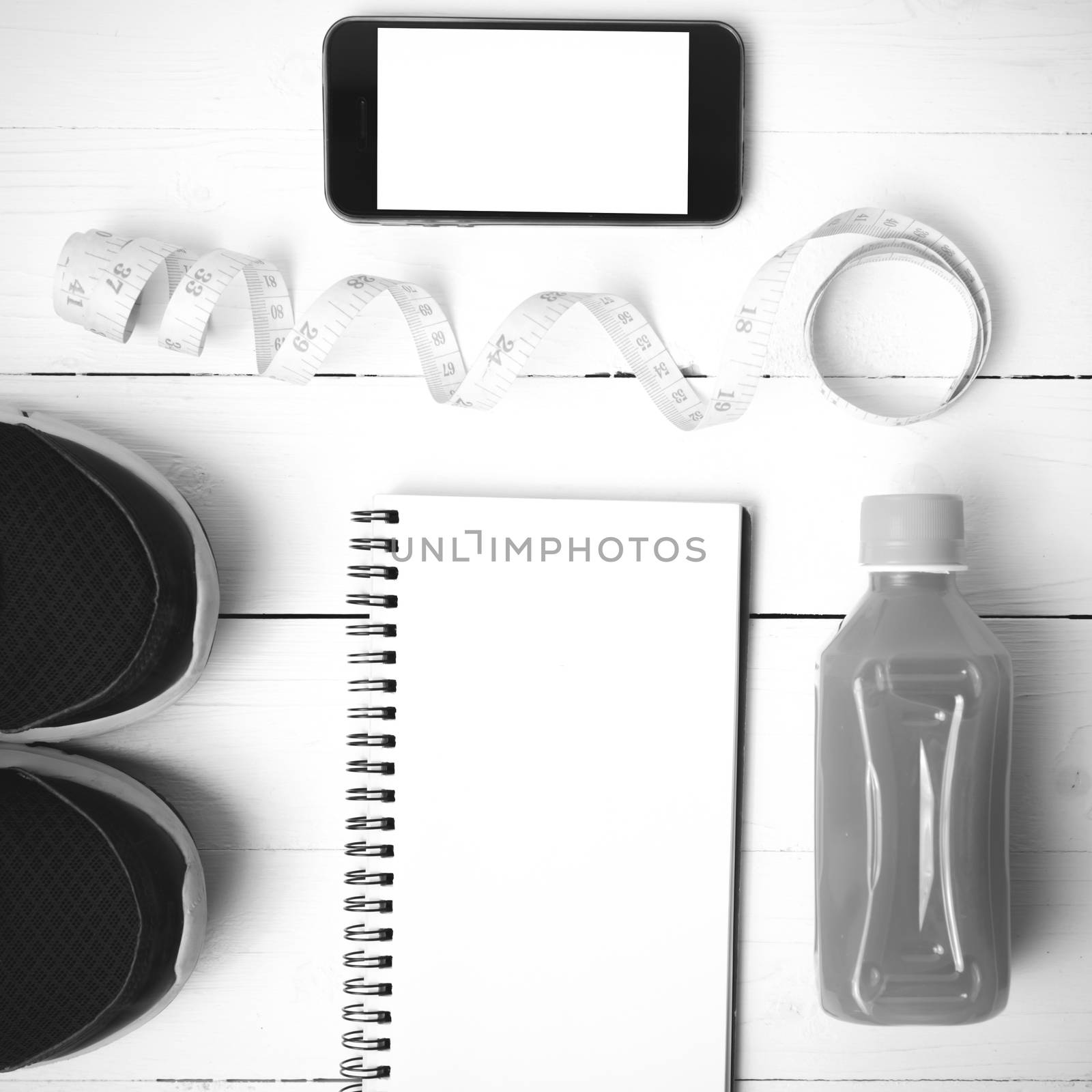 fitness equipment:running shoes,juice,measuring tape,notepad and phone on white wood background black and white color