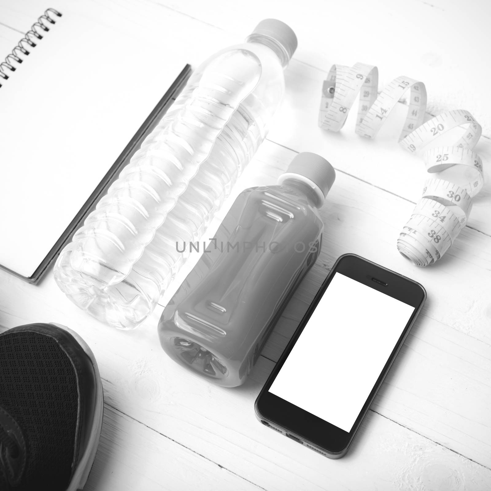 fitness equipment:running shoes,water,measuring tape,notepad,phone and juice on white wood background black and white color