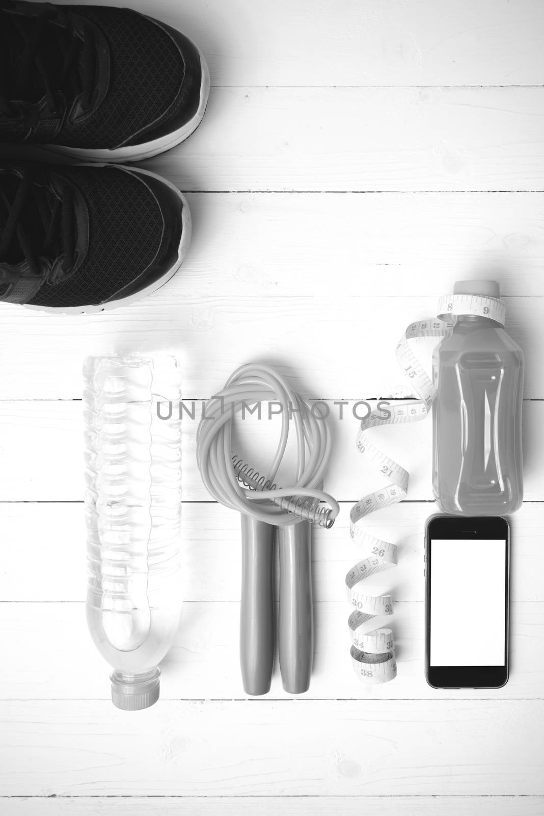 fitness equipment:running shoes,phone,measuring tape,water,juice and jumpong rope on white wood background black and white color