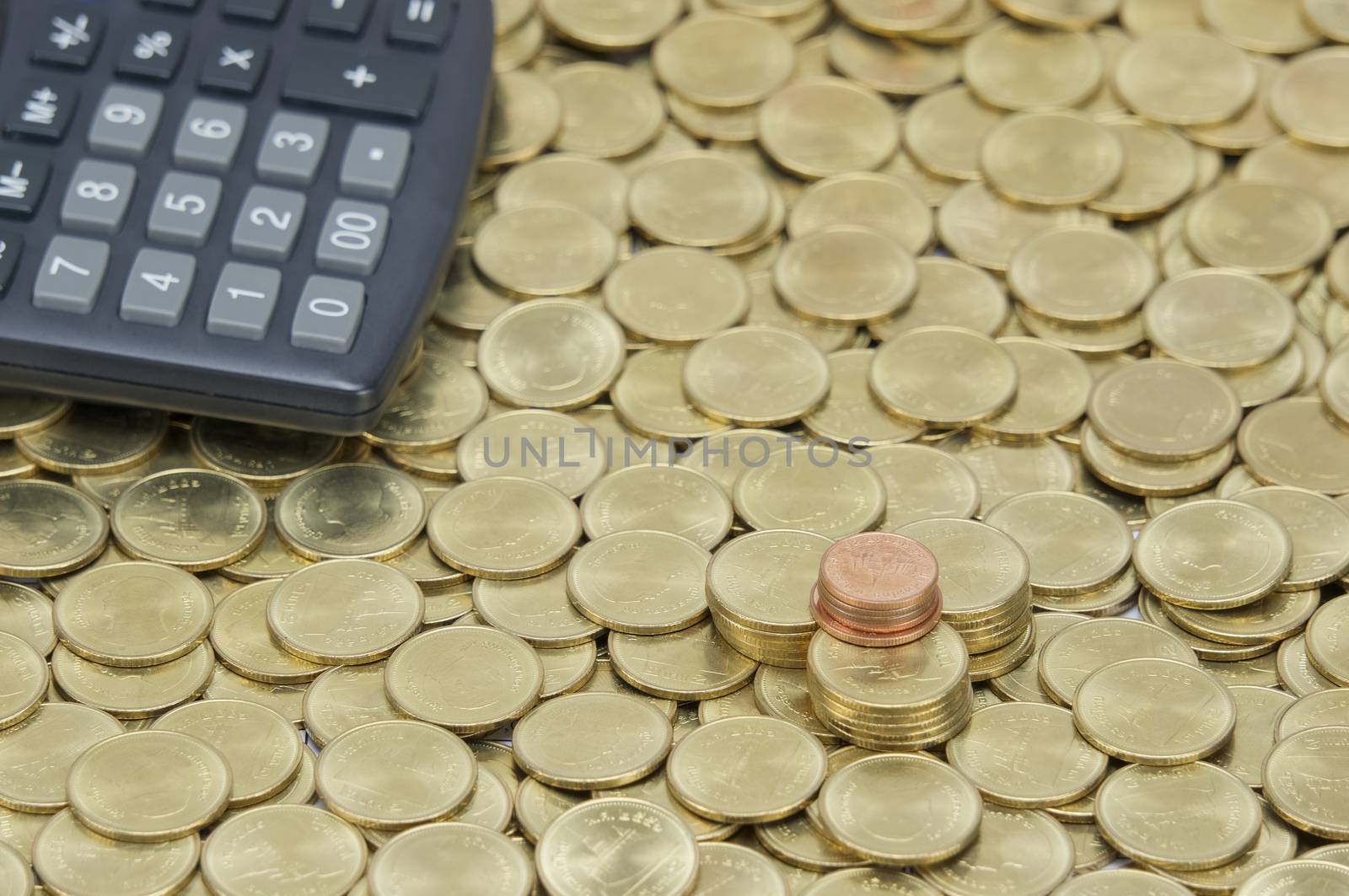 Pile of copper coins with calculator on stack of gold coins as background. 