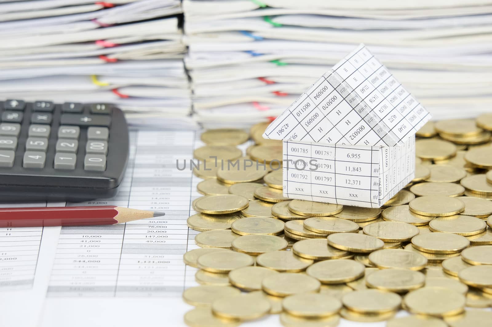 Pencil and calculator with house on stack of gold coins on another side on finance account have pile of document as background.