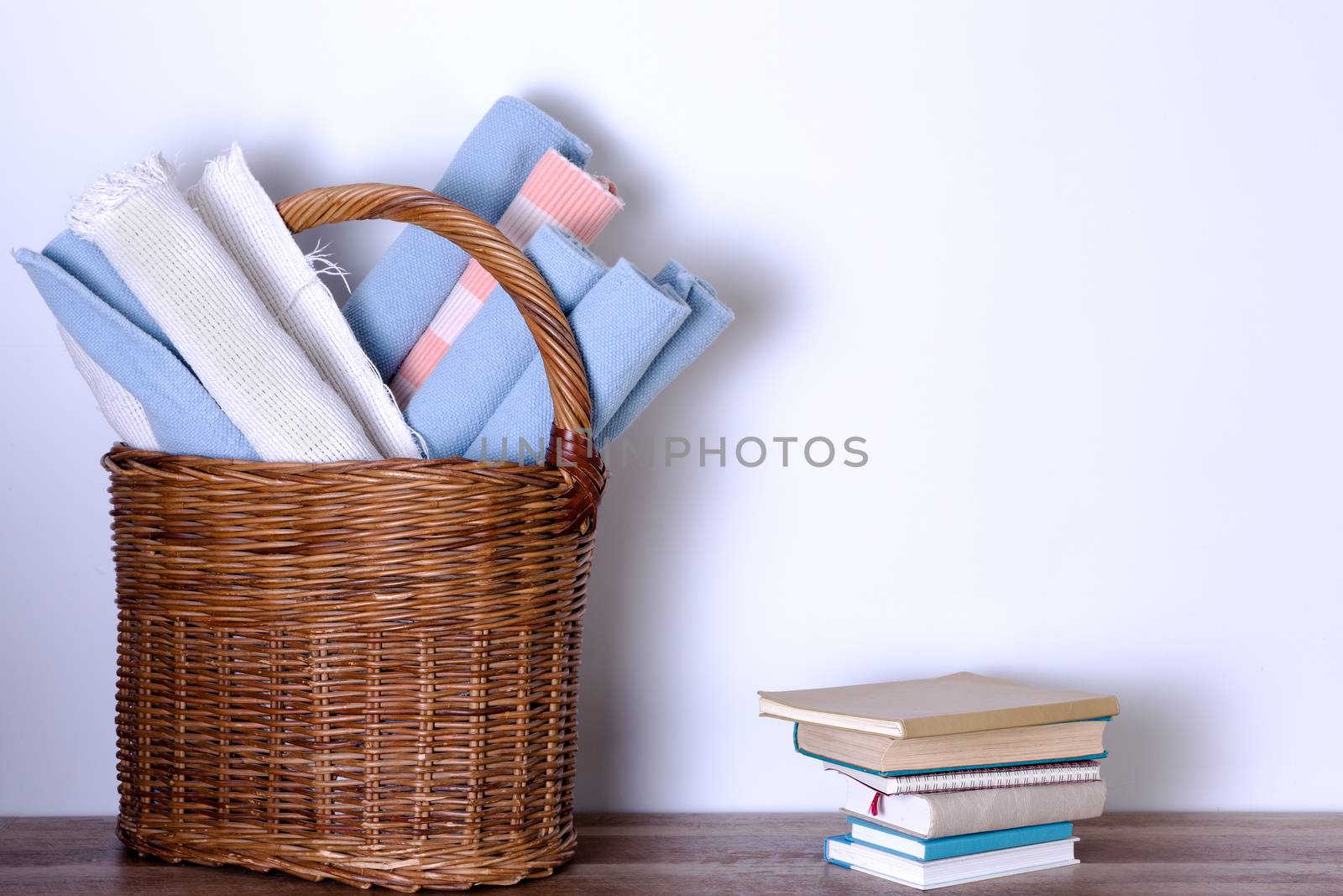 Worn Out School Rugs in a Basket and Piled Books Against White Wall with Copy Space.