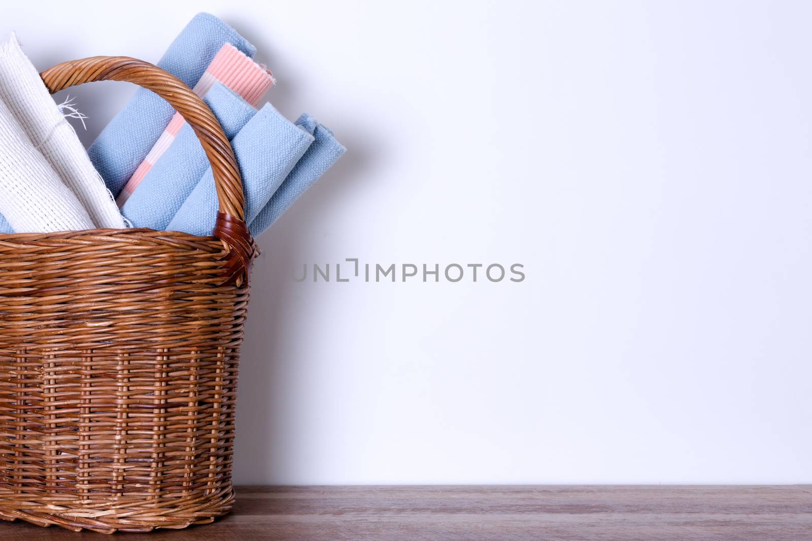 Assorted Worn Out School Rugs in a Wooden Basket Against White Wall with Copy Space.