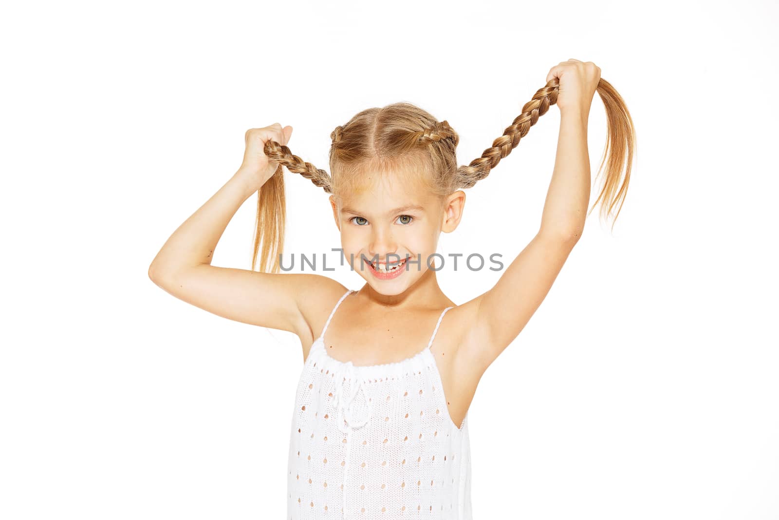 Funny little girl with a charming smile in a white dress holding a pigtails
