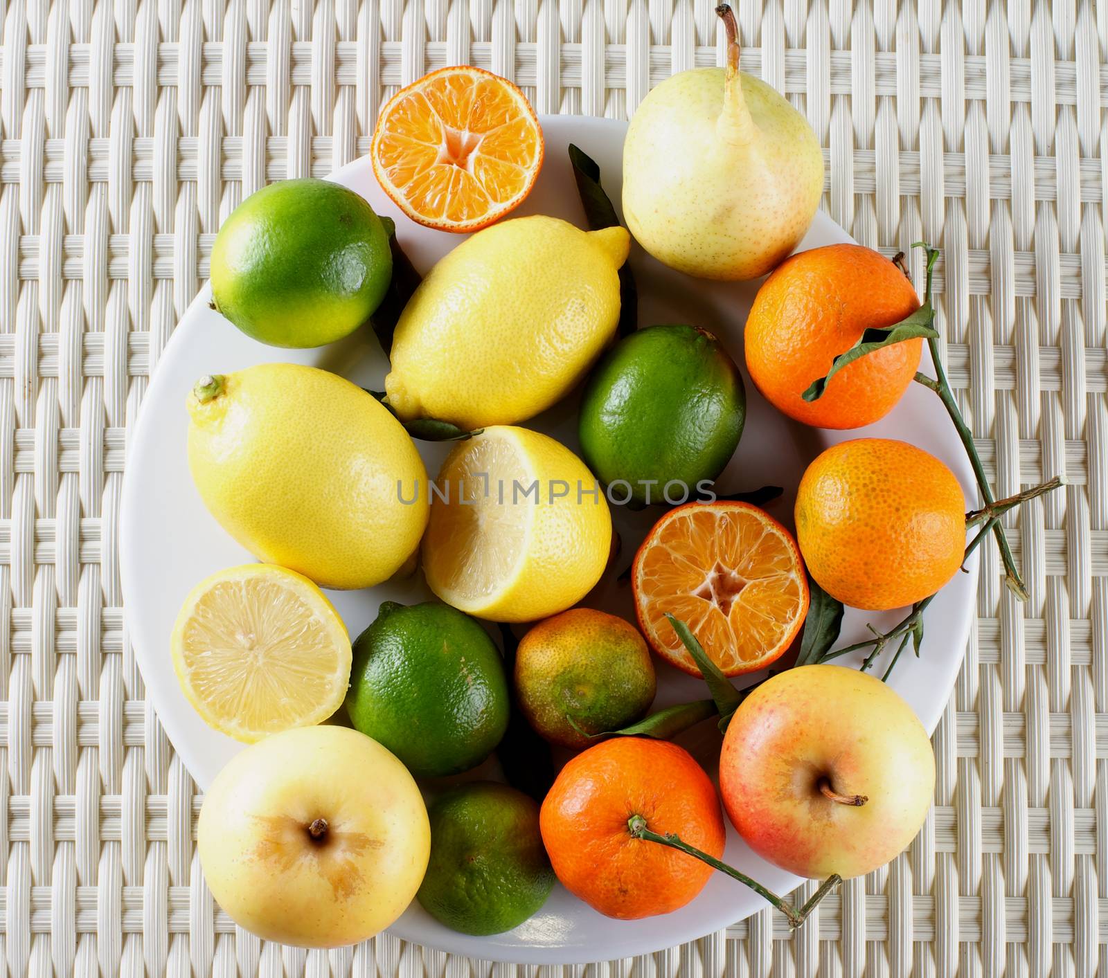 Big Plate with Fresh Ripe Lemons, Limes, Oranges, Tangerines, Yellow Apples and White Pears on Wicker background. Top View