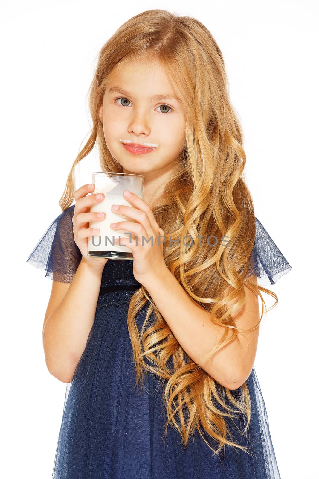 Cute little girl with blond hair in a blue dress holding a glass of milk