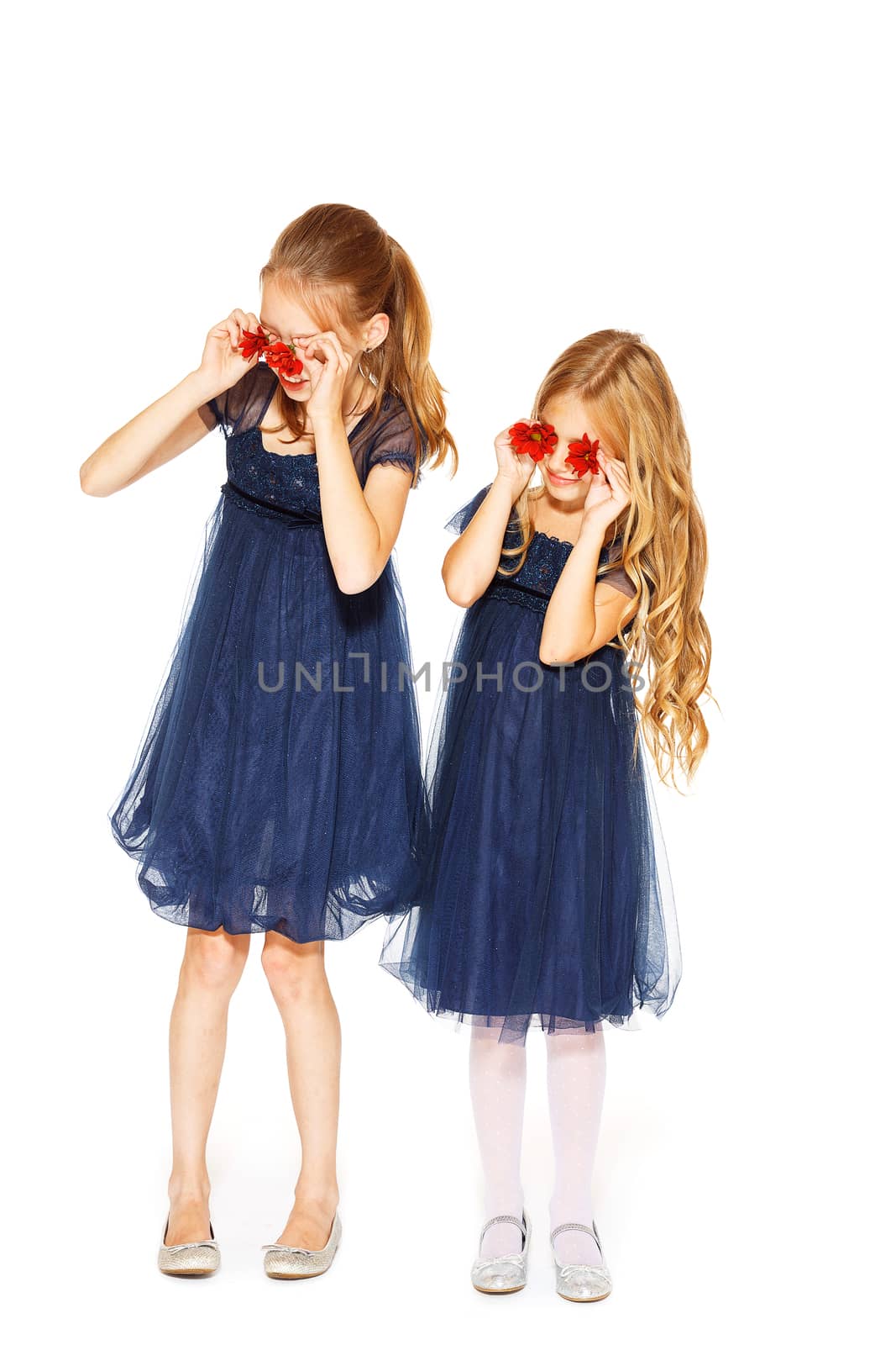Little cute girls holding two red flowers near their eyes