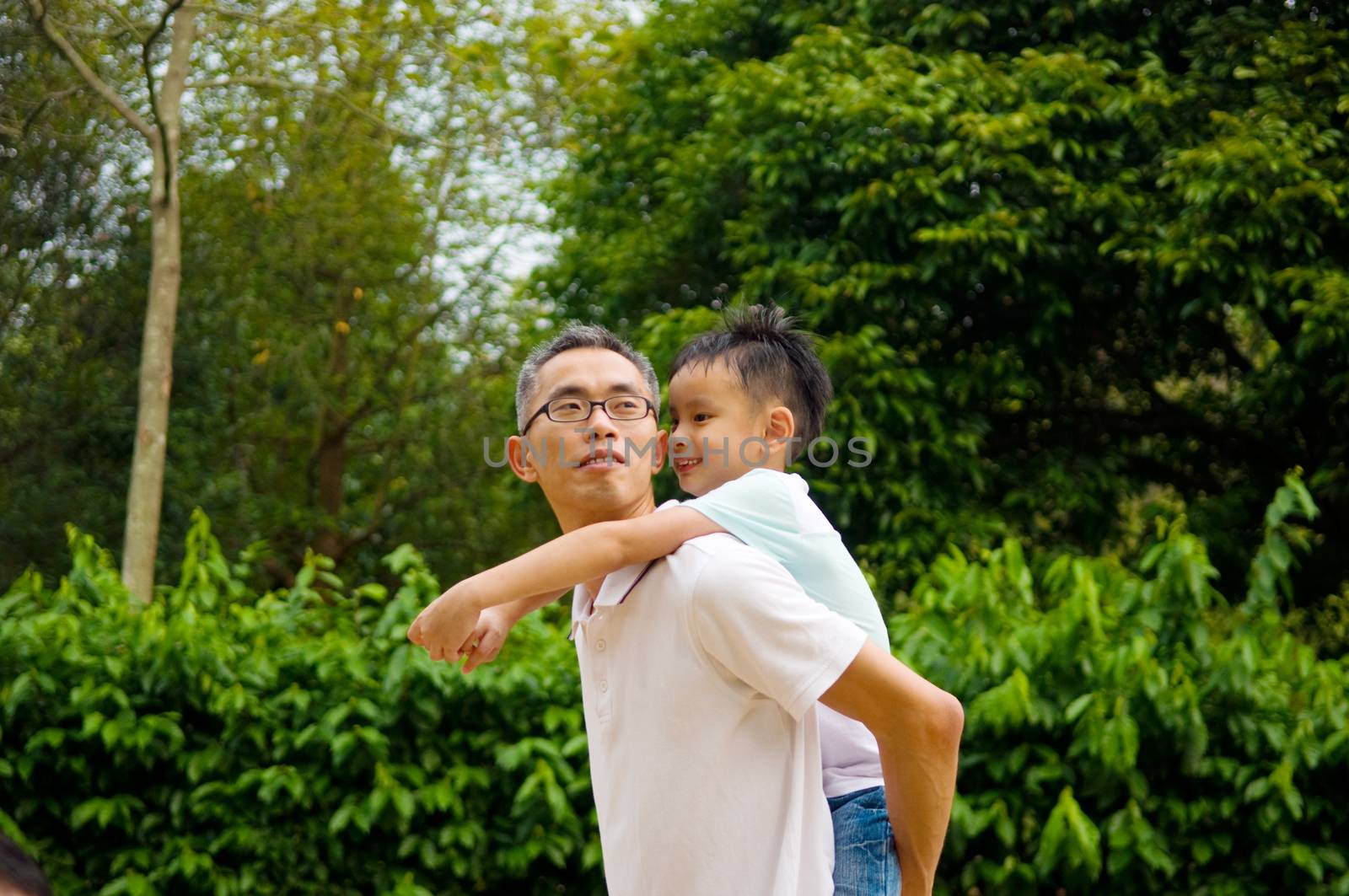 Asian father giving piggyback ride to his son in the evening sunshine